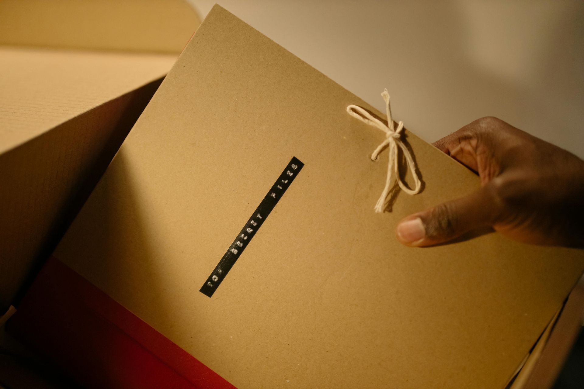 A hand pulls a brown folder with text and string tie from a box.