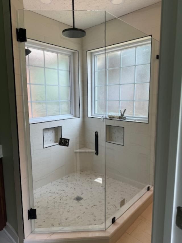 A bathroom with a walk in shower with a glass door and a window.