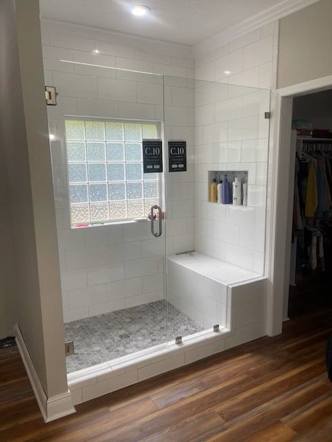 A bathroom with a walk in shower with a bench and a window.