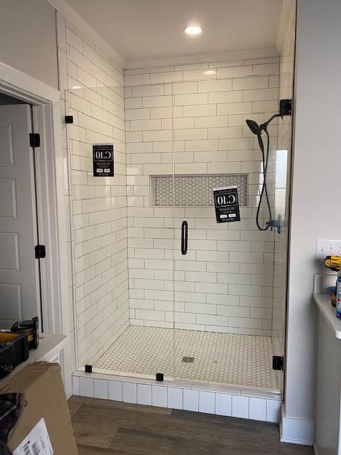 A bathroom with a walk in shower with white tiles and a glass door.