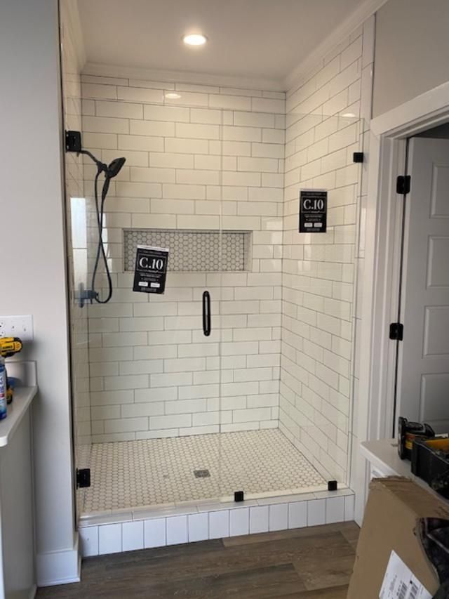 A bathroom with white tiles and a walk in shower with a glass door.
