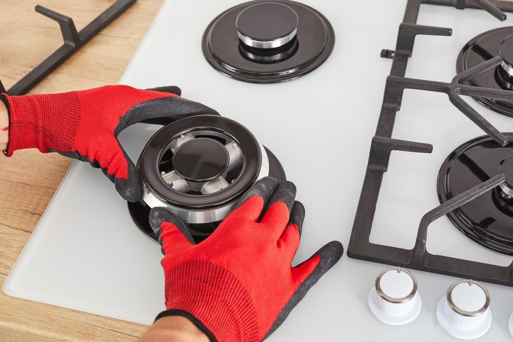Hands in Red Gloves Installing a Stovetop Burner — JMJ Plumbing and Electrical NSW In Tumbi Umbi, NSW