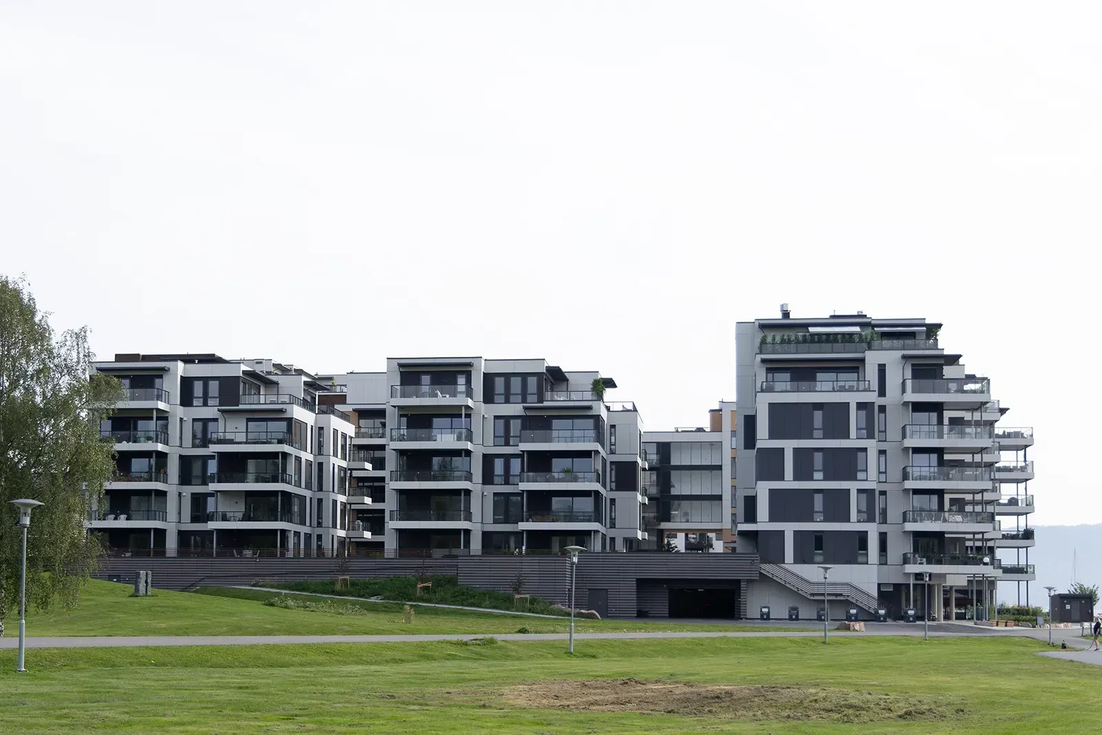 Boligblokker i Bryggeparken med utkragede balkonger, fasade i lyse og mørke Equitone-plater og utsyn mot grøntområde