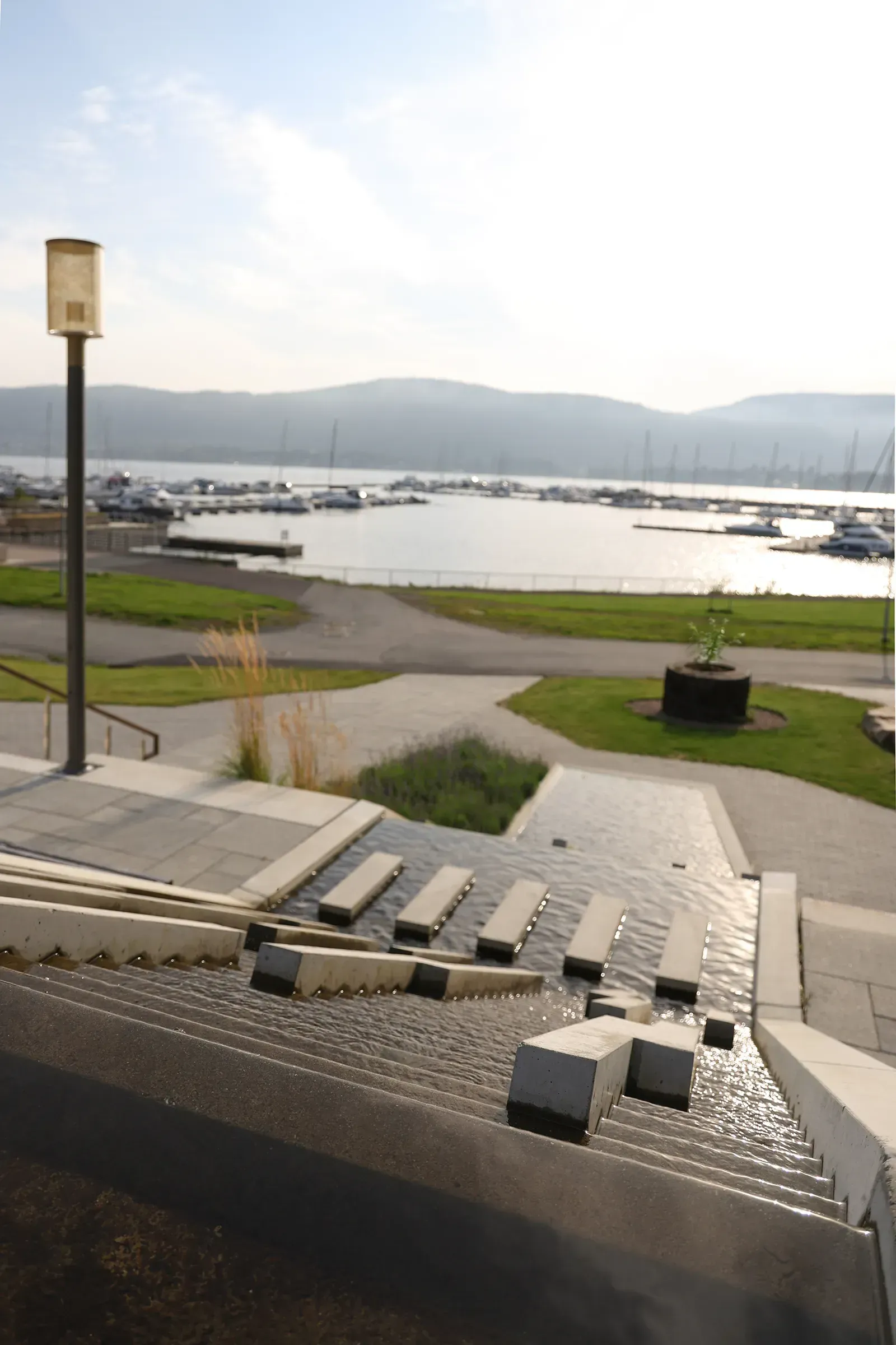 Trappeanlegg med vannrenner ned mot fjorden, utsikt over marina og åslandskap.