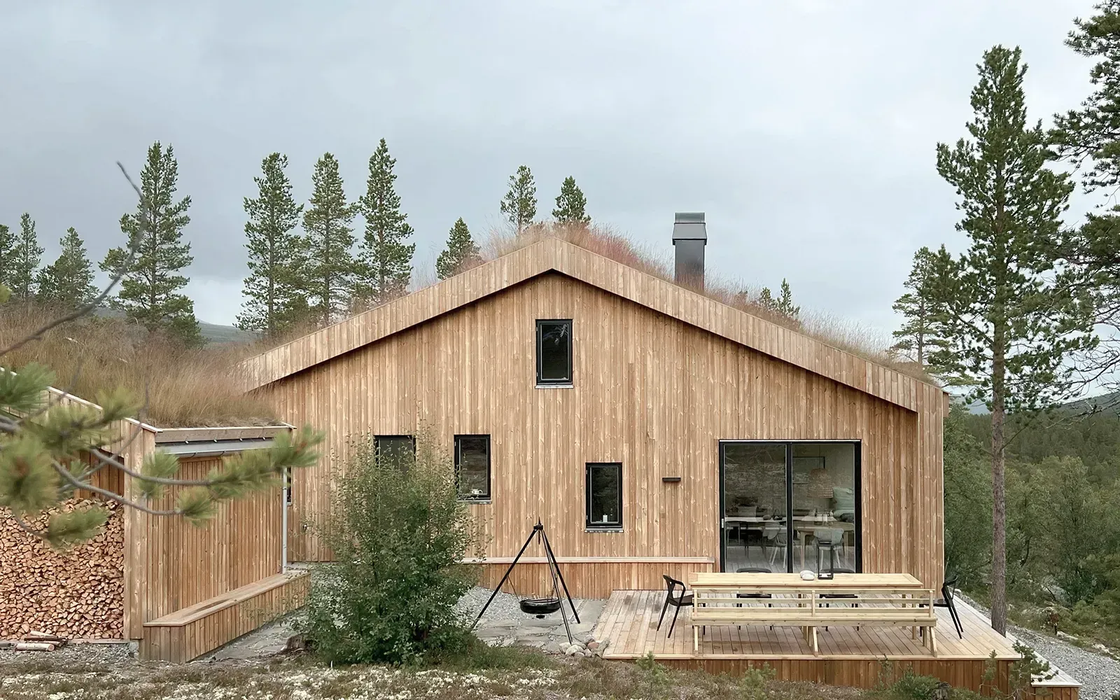 Moderne hytte i Jotunheimen med trekledning, gresskledd saltak, store glasskyvedører og integrert uteplass i treverk