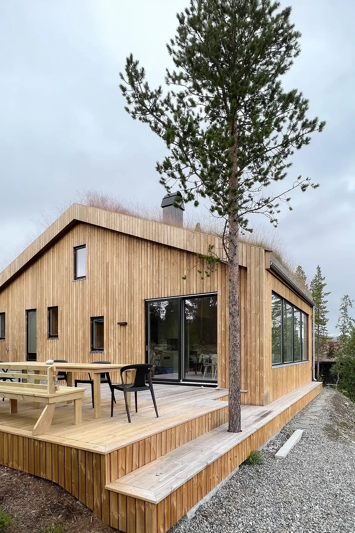Detalj av hjørnefasade med store glassflater og terrasse i treverk, som åpner hytta opp mot naturen.