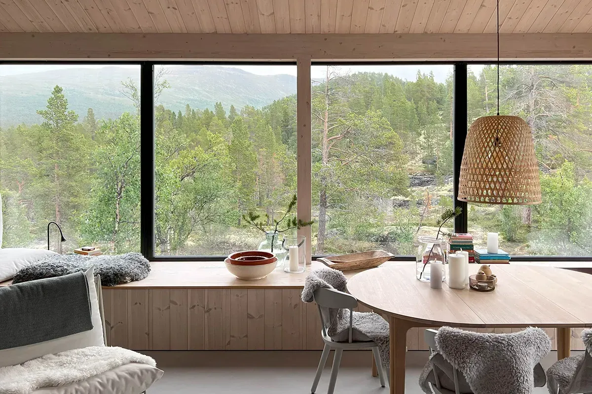 Spiseplass med panoramautsikt mot Jotunheimen gjennom store glassflater, omgitt av lyst treverk og enkle, nordiske møbler.
