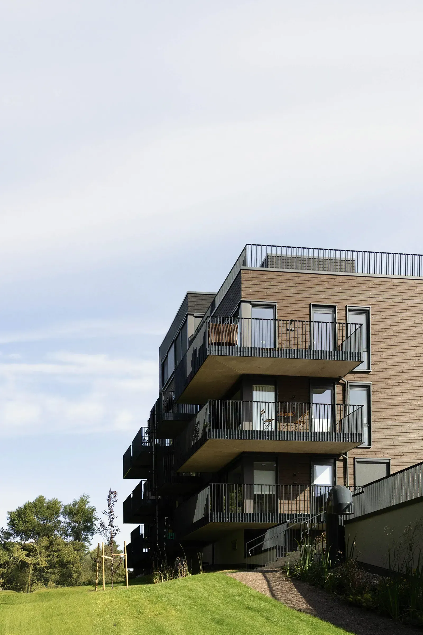 Gavlfasade i Østensjøporten med åpne balkonger, store vindusfelt og trekledning i varme jordtoner mot uteareal