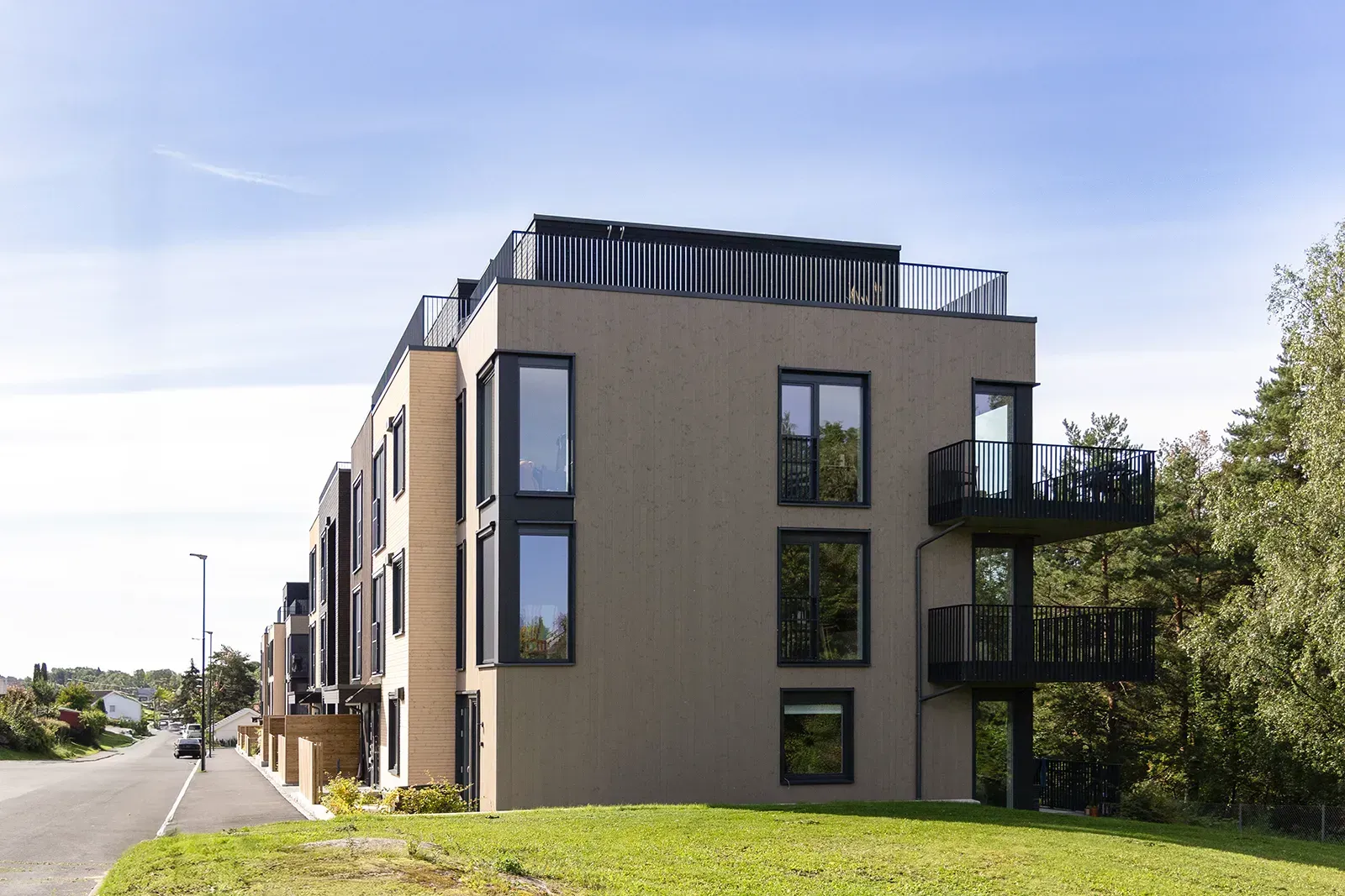 Moderne boligbygg i tre med store vindusflater, balkonger og takterrasse mot grøntareal.