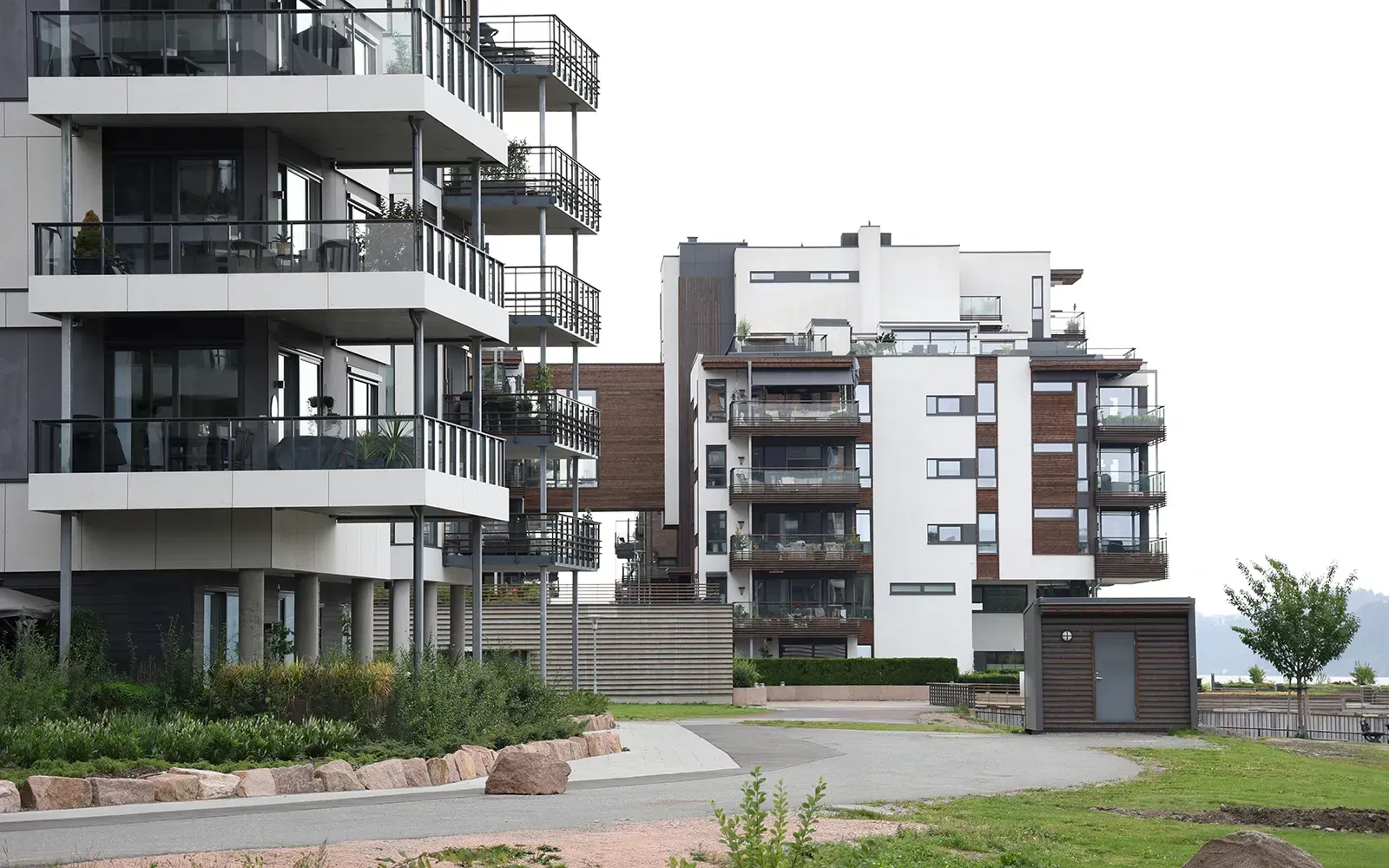 Boligbebyggelse i Utsikten sett fra gangvei, med hvit puss, mørk tre, store vinduer og balkonger med tre- og glassdetaljer