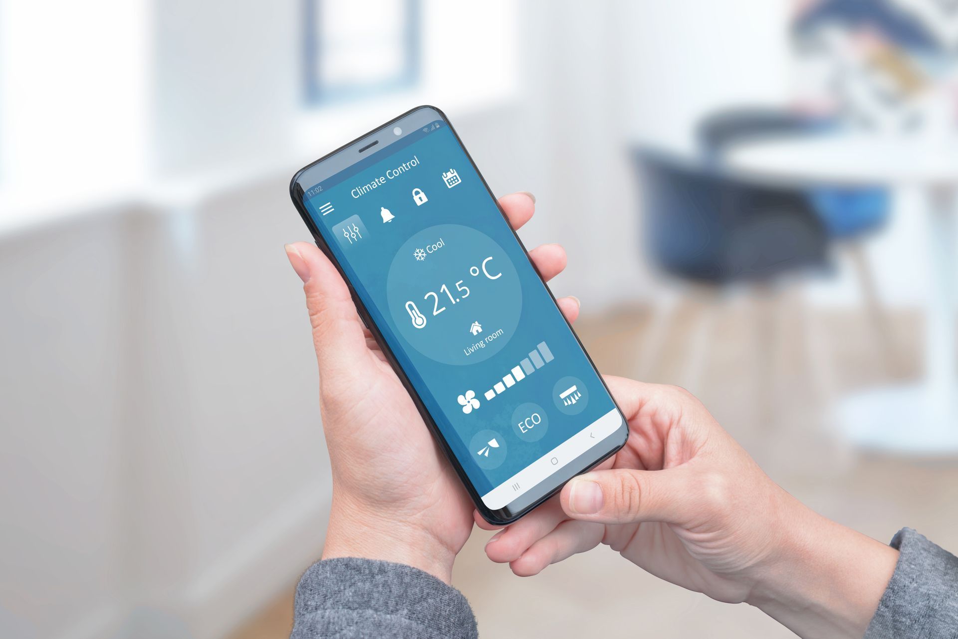 Person holding a smartphone showing a smart thermostat app with a blue interface.