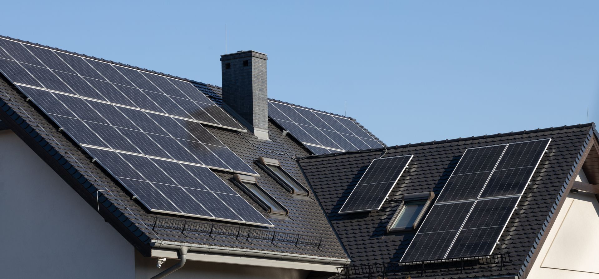 Roof of a house covered in solar panels, with a chimney and clear blue sky.