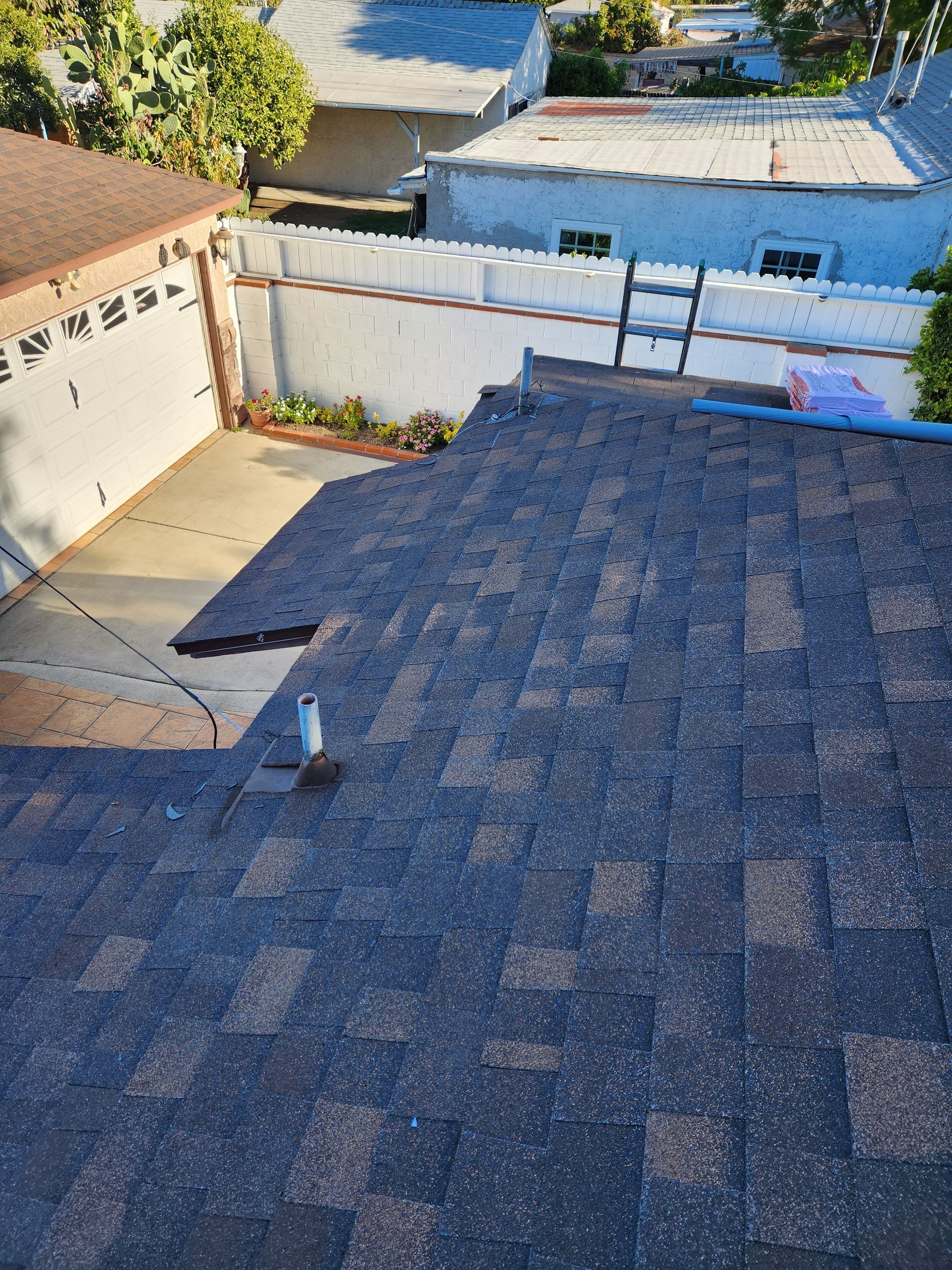 High-angle view of a dark shingled roof, a white garage, and a fenced yard with a small garden area.