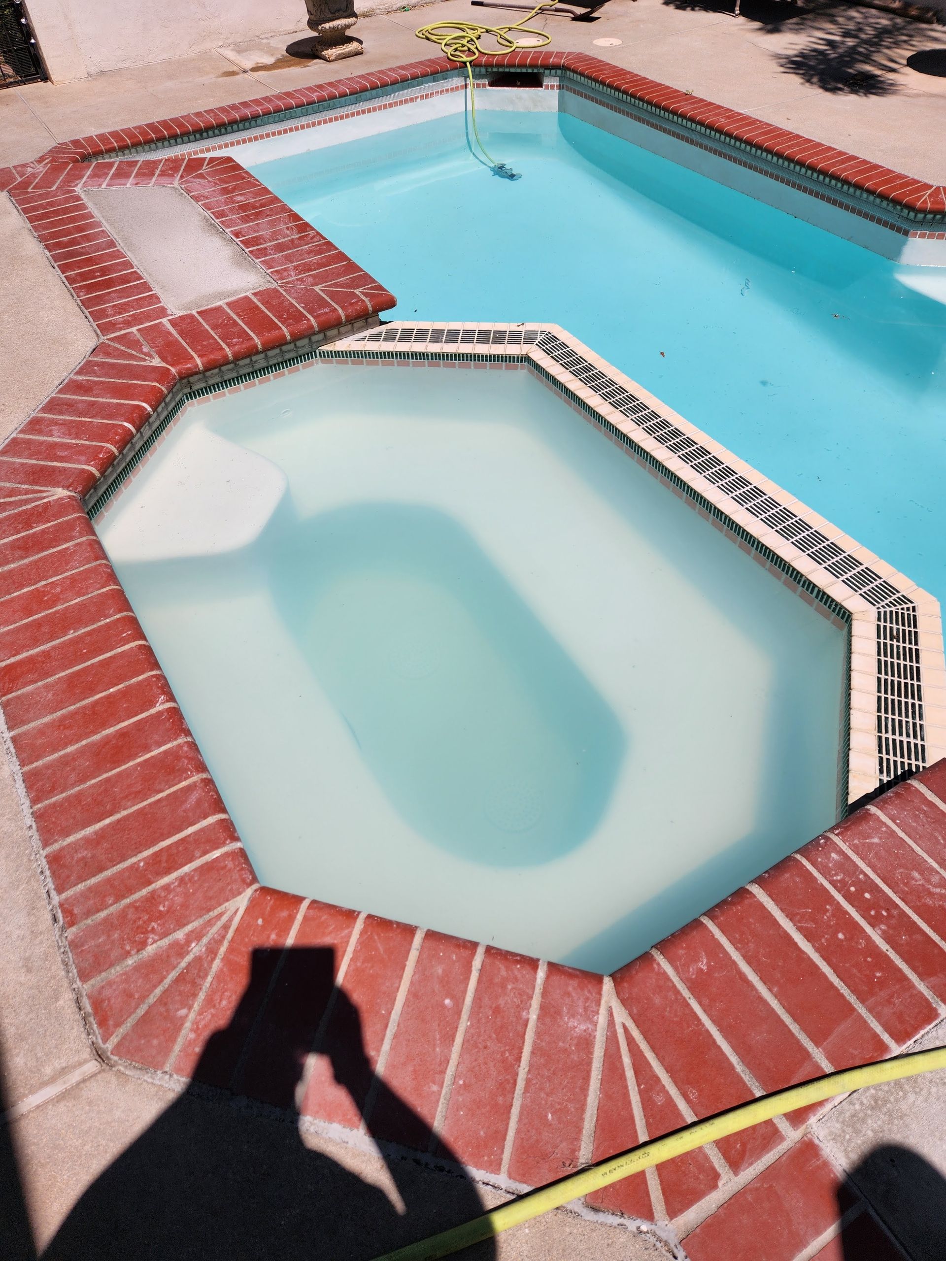 Swimming pool and spa with brick coping. Water is light blue. Shadow of person taking the photo.