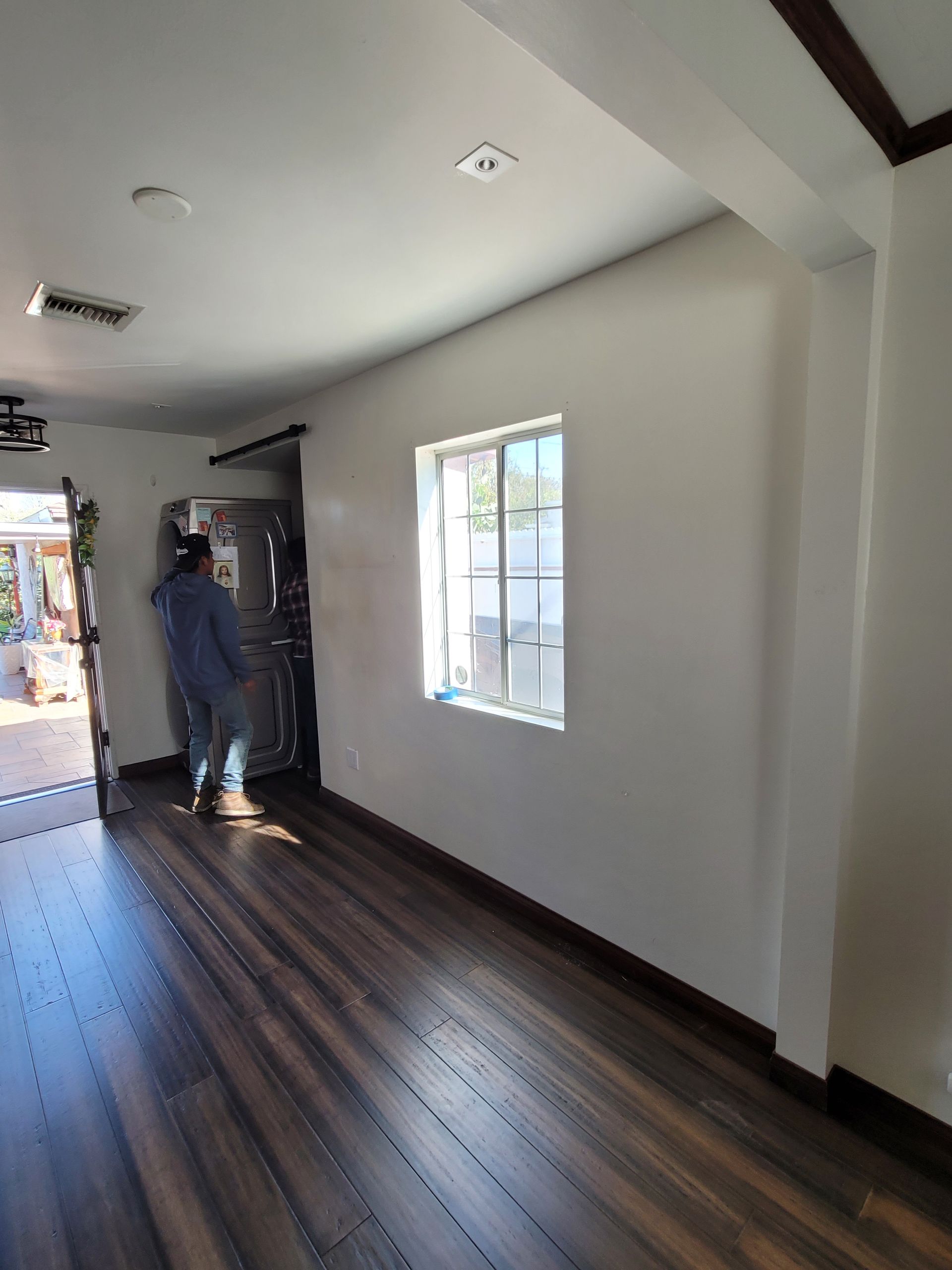 A man is standing in a room with hardwood floors and a window.