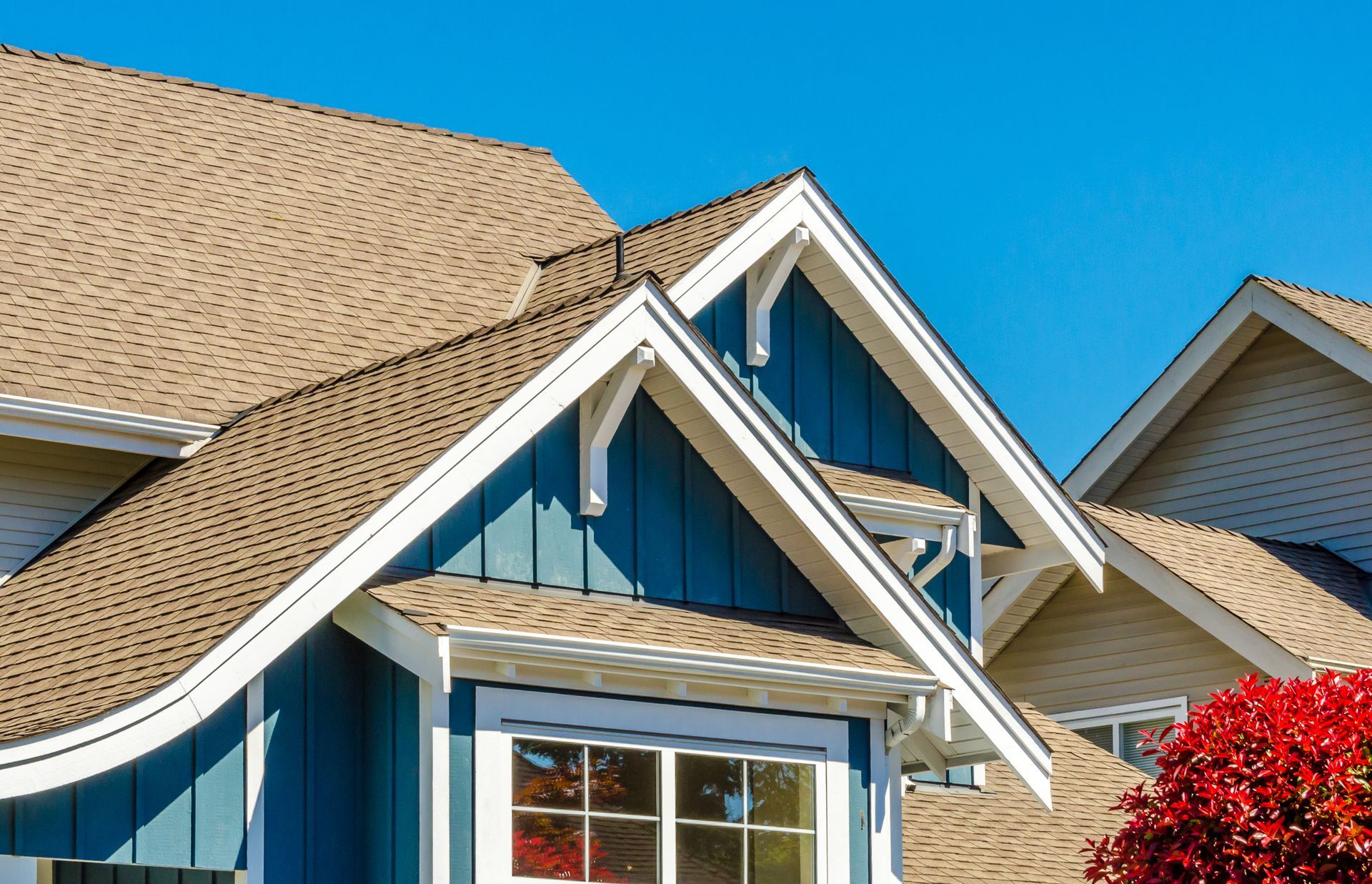 Blue house exterior with brown roof and white trim against a clear blue sky.