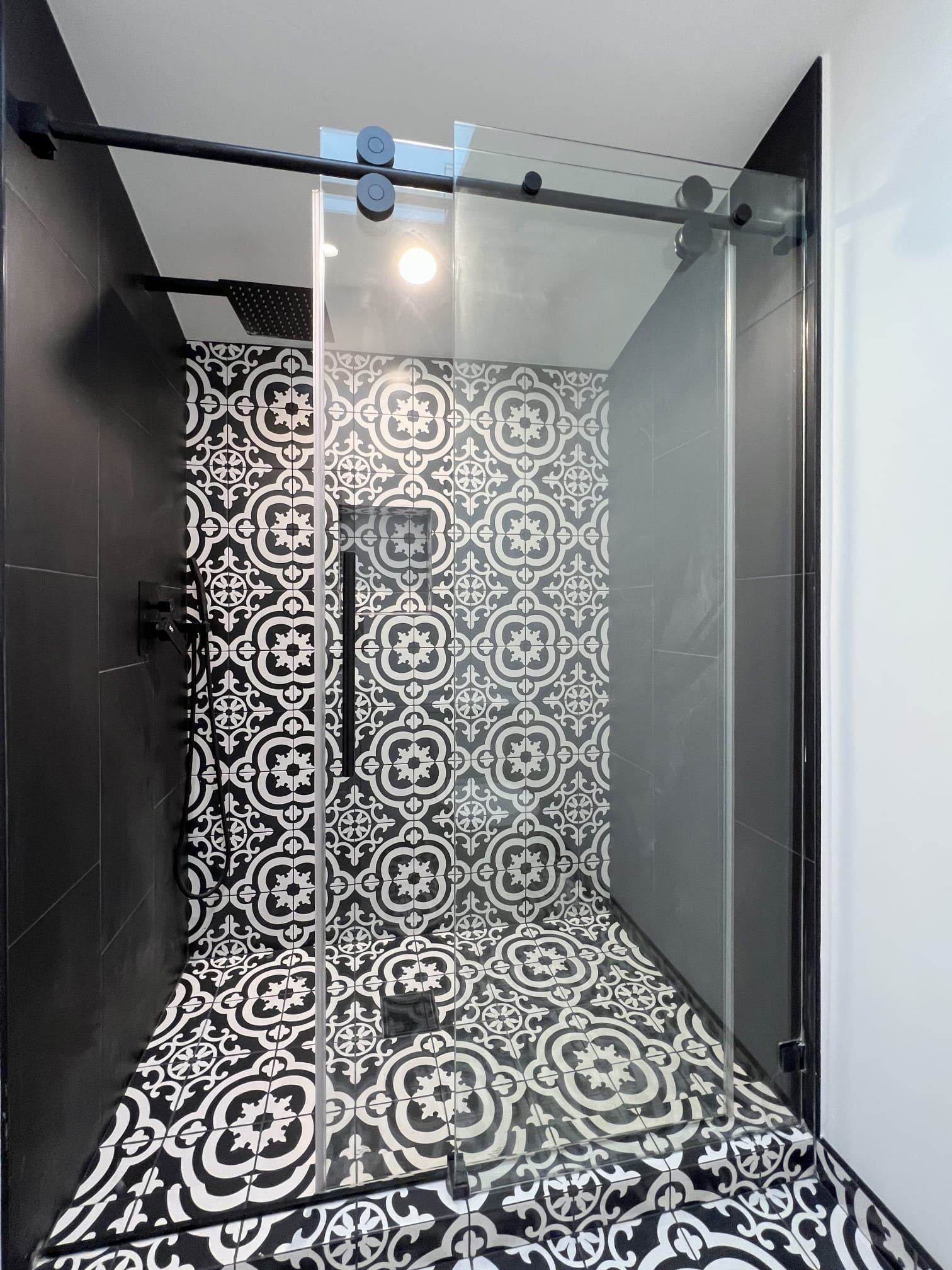 A modern glass-enclosed shower with bold, black-and-white patterned tile walls and floors and matte black fixtures.