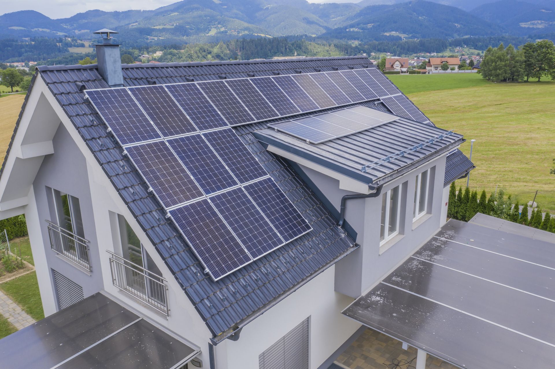 House with gray roof tiles and solar panels, mountains in the background.