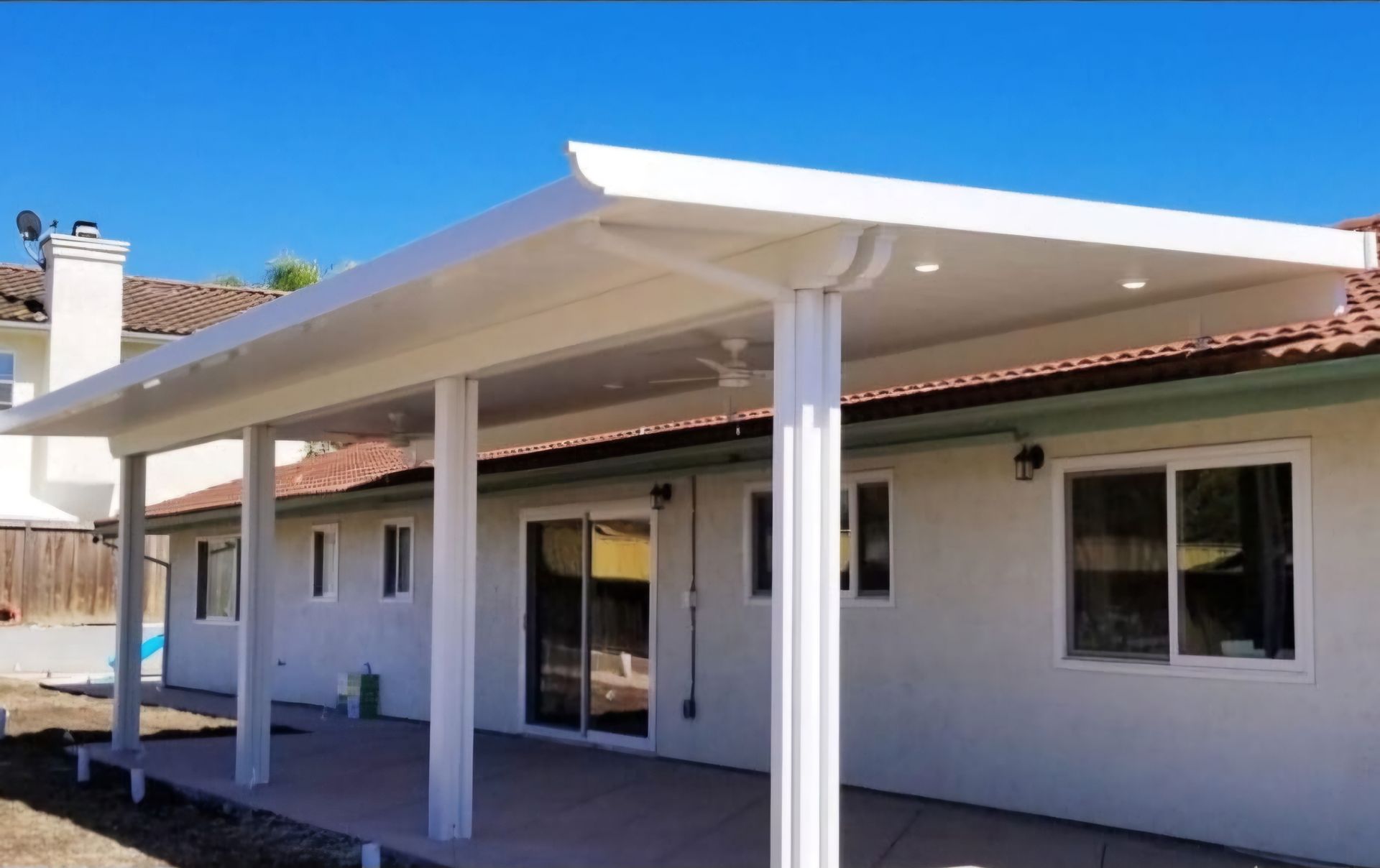 White patio cover extending from a beige house with blue sky background.