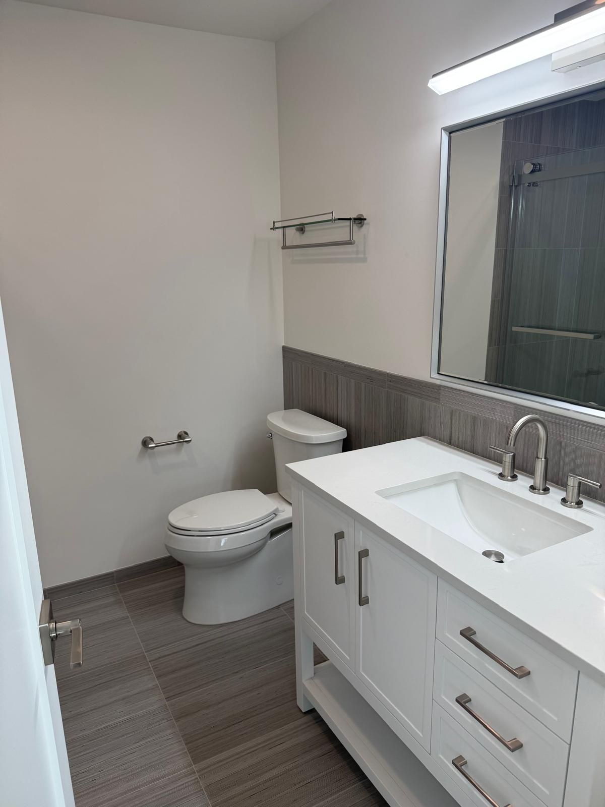 A bathroom with a toilet , sink and mirror.