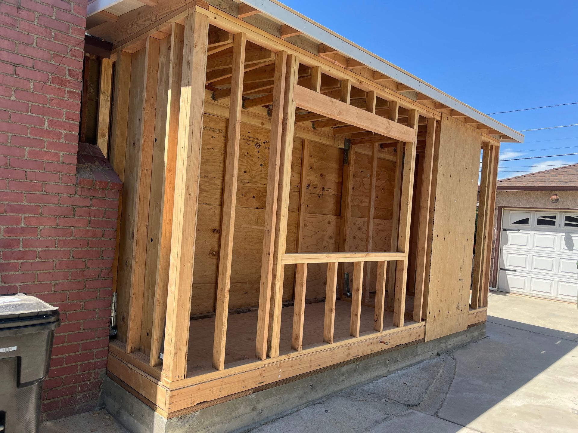 Exterior wooden structure in progress, attached to a brick wall. A window frame is visible.