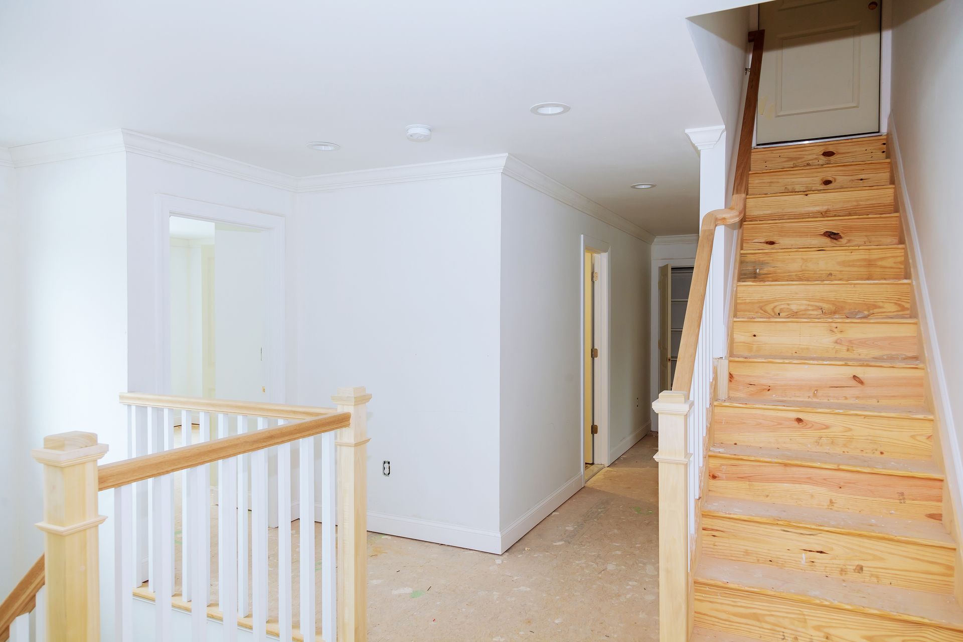 Hallway with unfinished staircase and doorway, light wood and white walls.