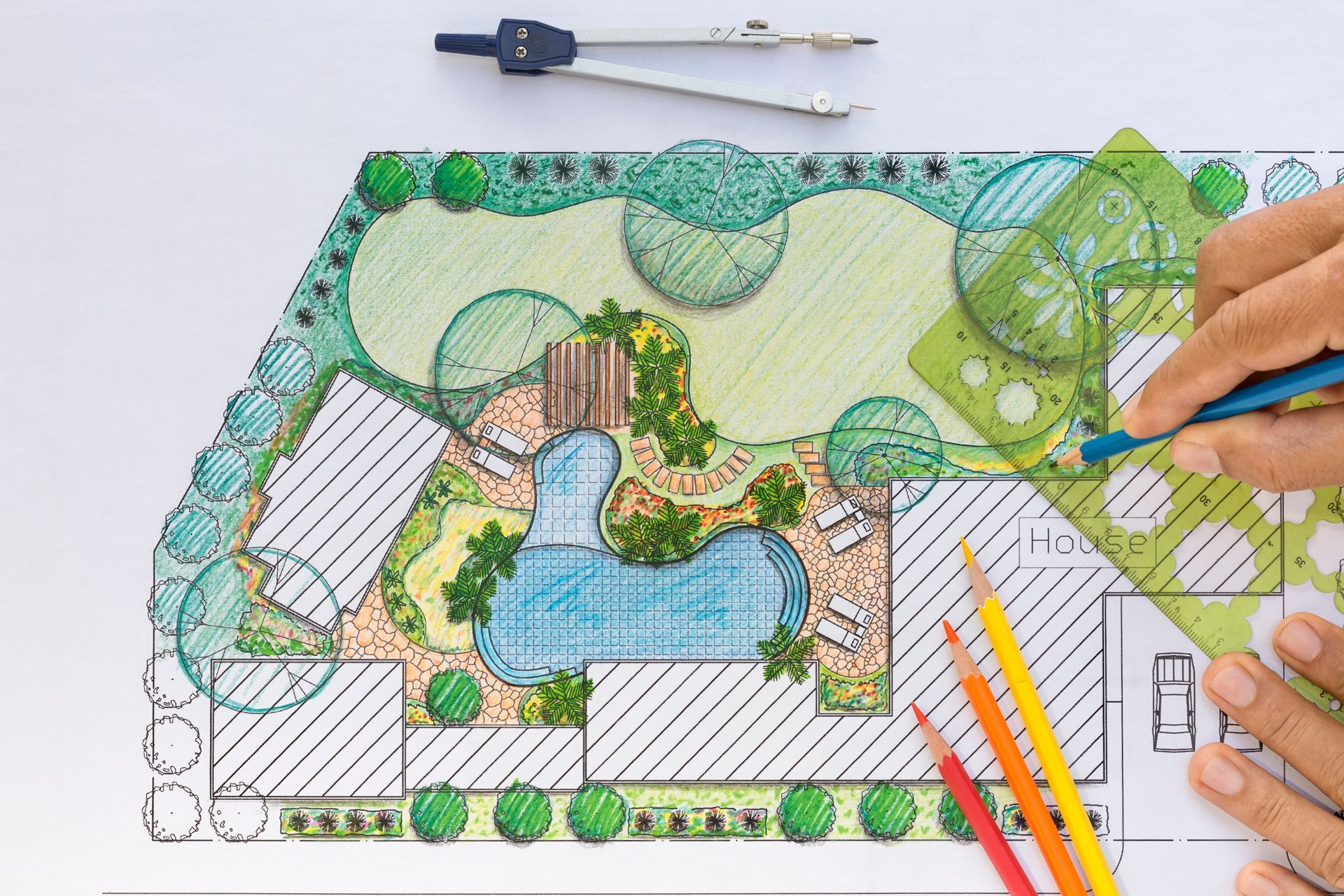 A person is drawing a garden plan with a compass and pencils.