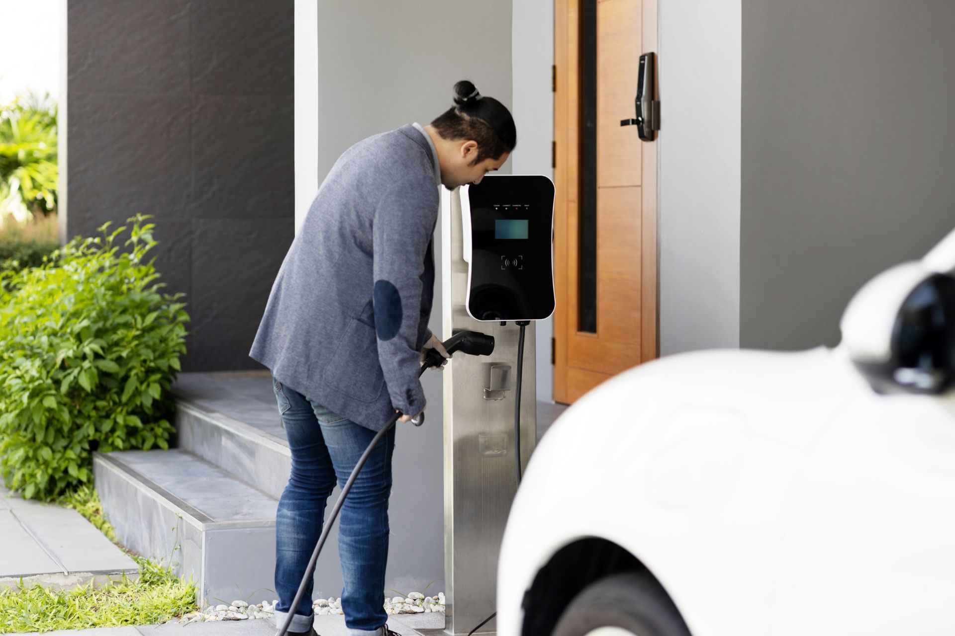 Person plugging an electric vehicle into a charging station next to a house.