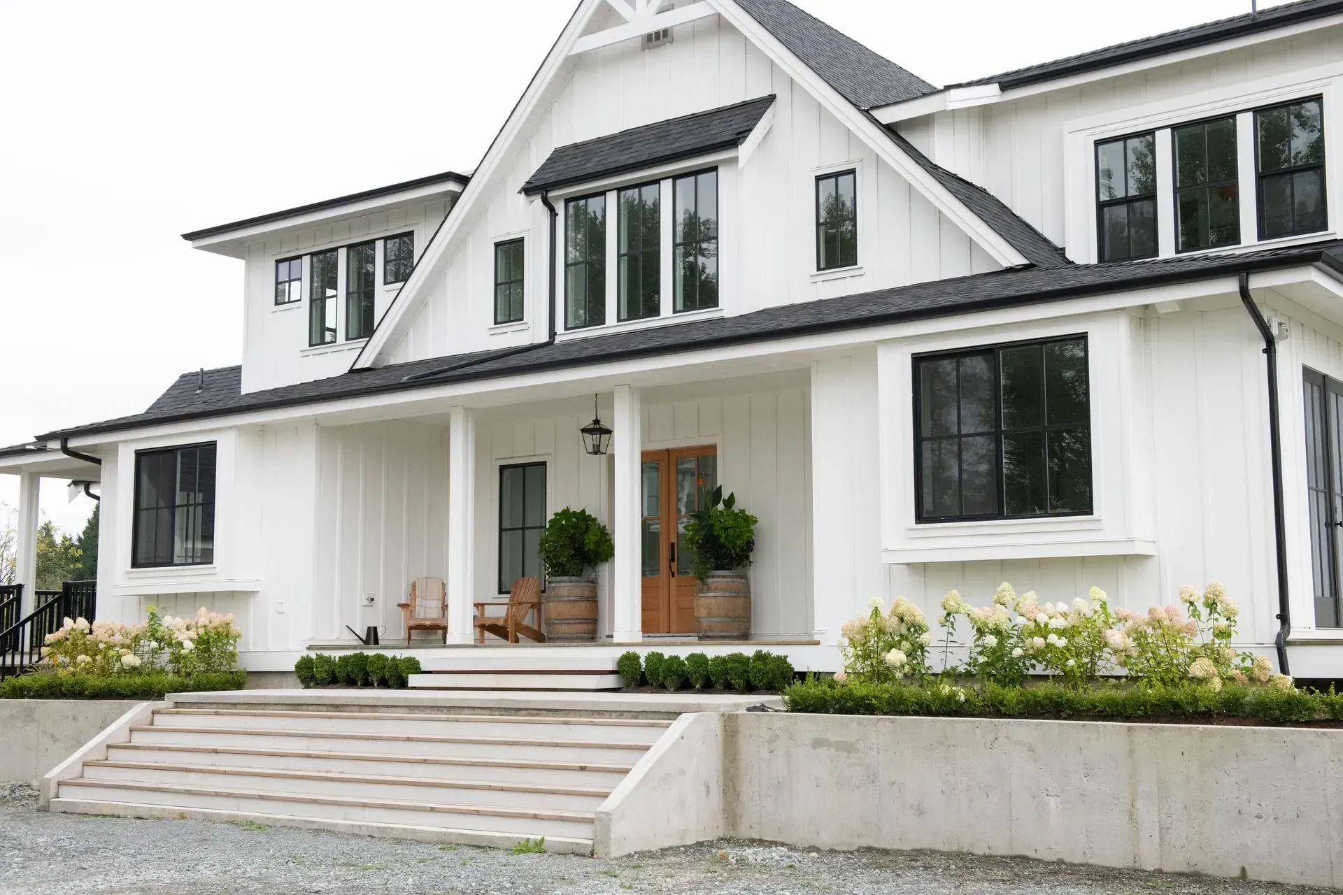 White farmhouse with black windows and roof, featuring a porch and landscaping.