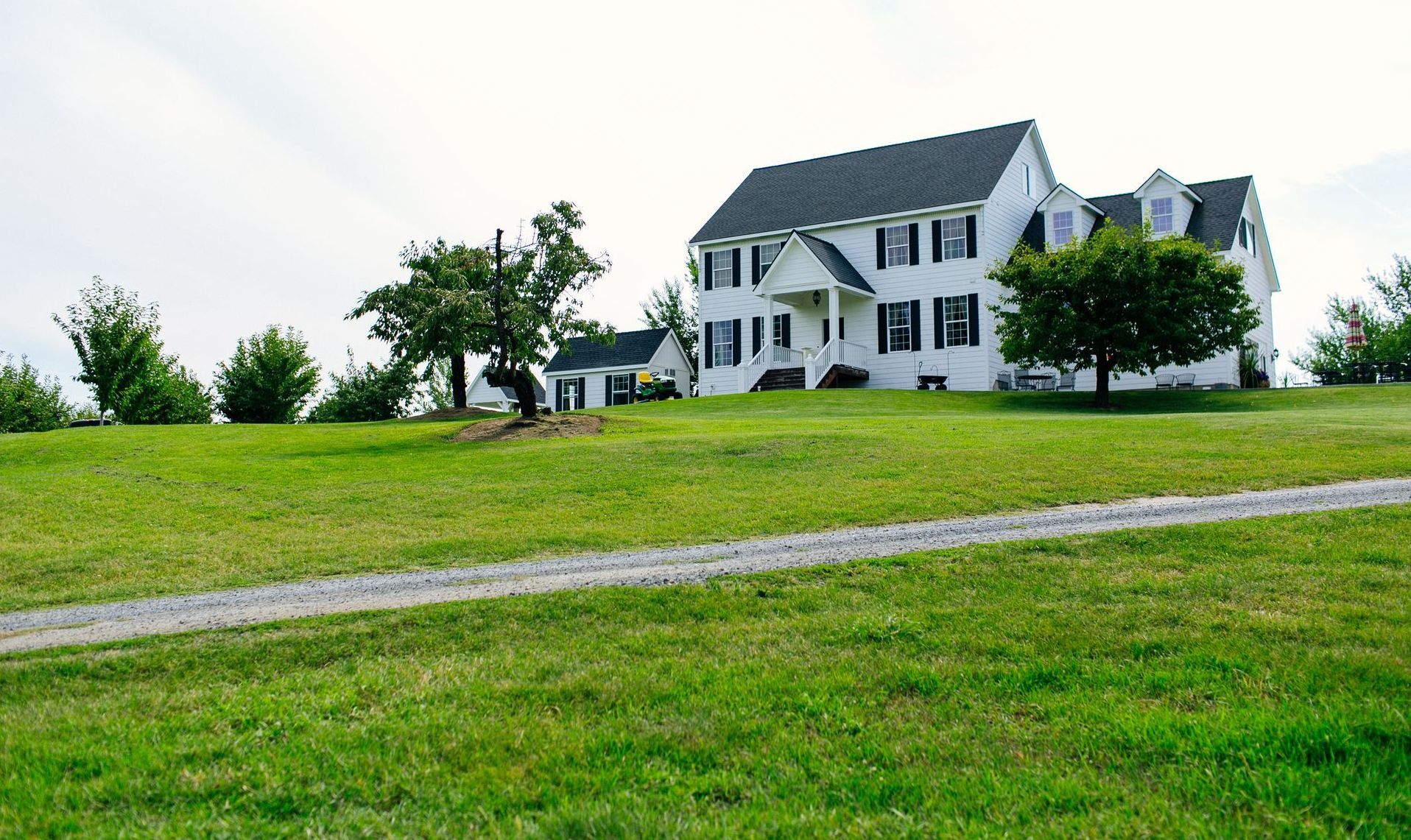 A large white house is sitting on top of a lush green hill.