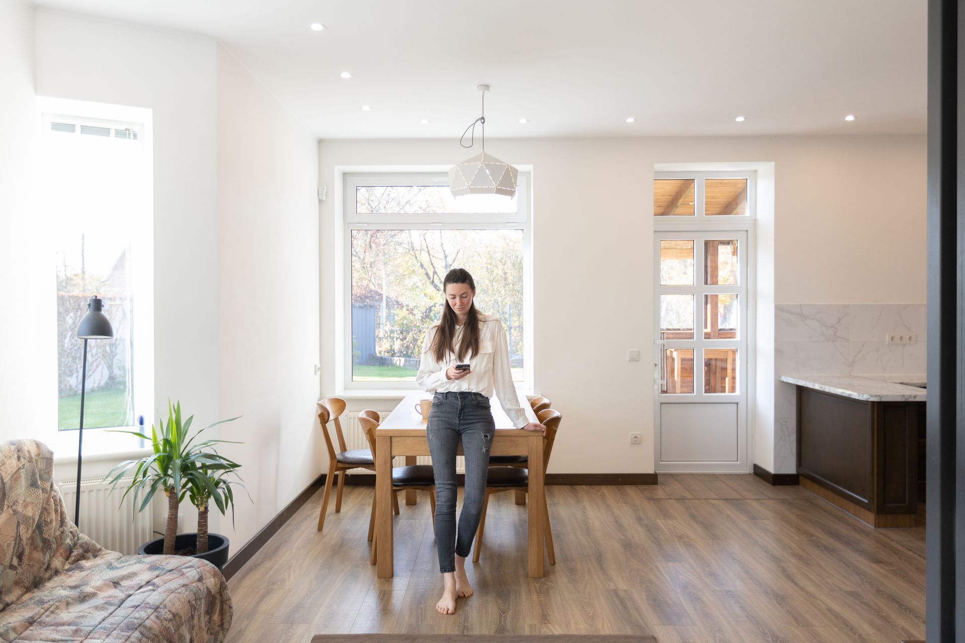 A woman is standing in a living room looking at her phone.