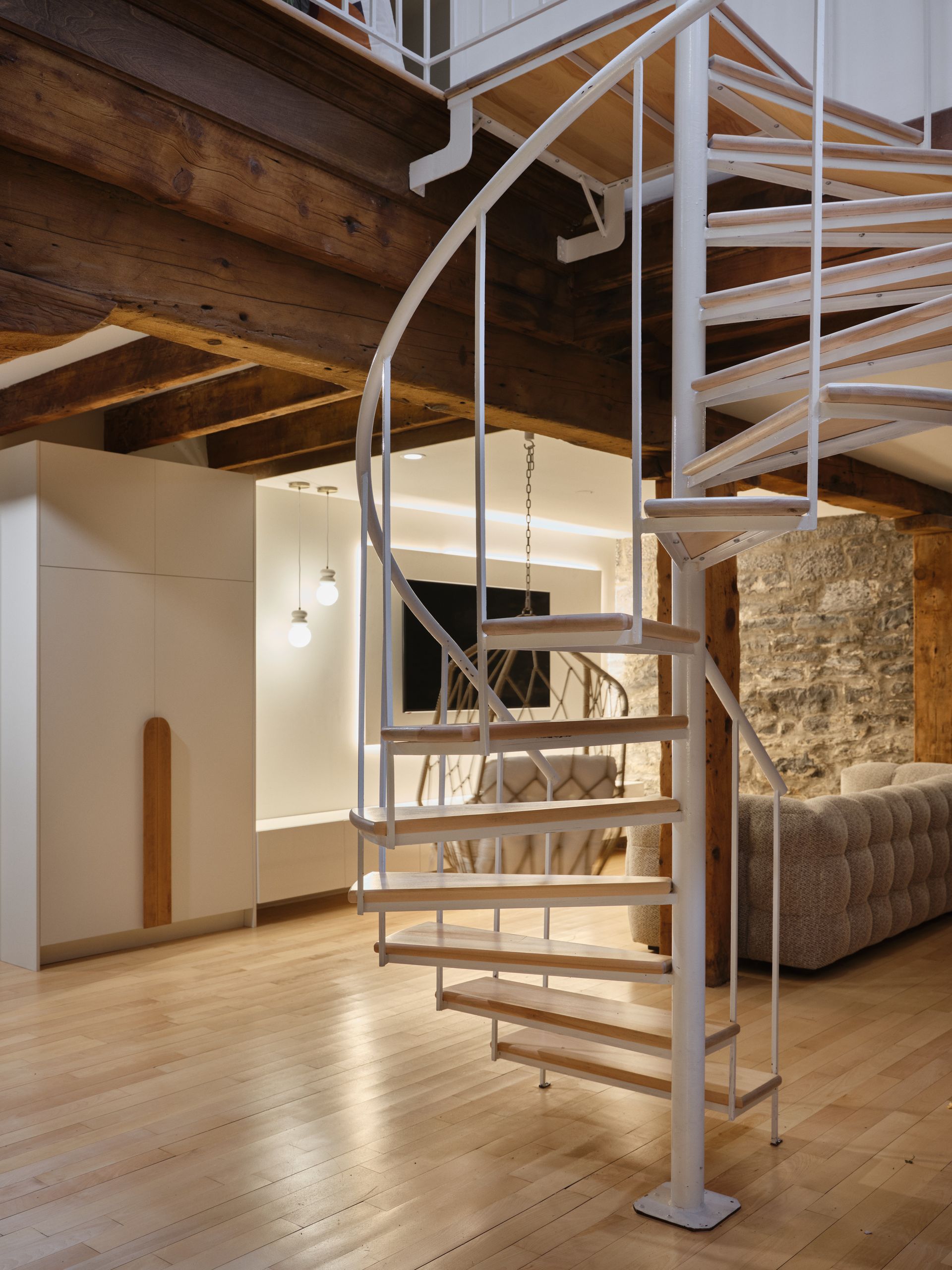 Escalier en colimaçon avec rampe blanche et marches en bois, dans une pièce au parquet clair.
