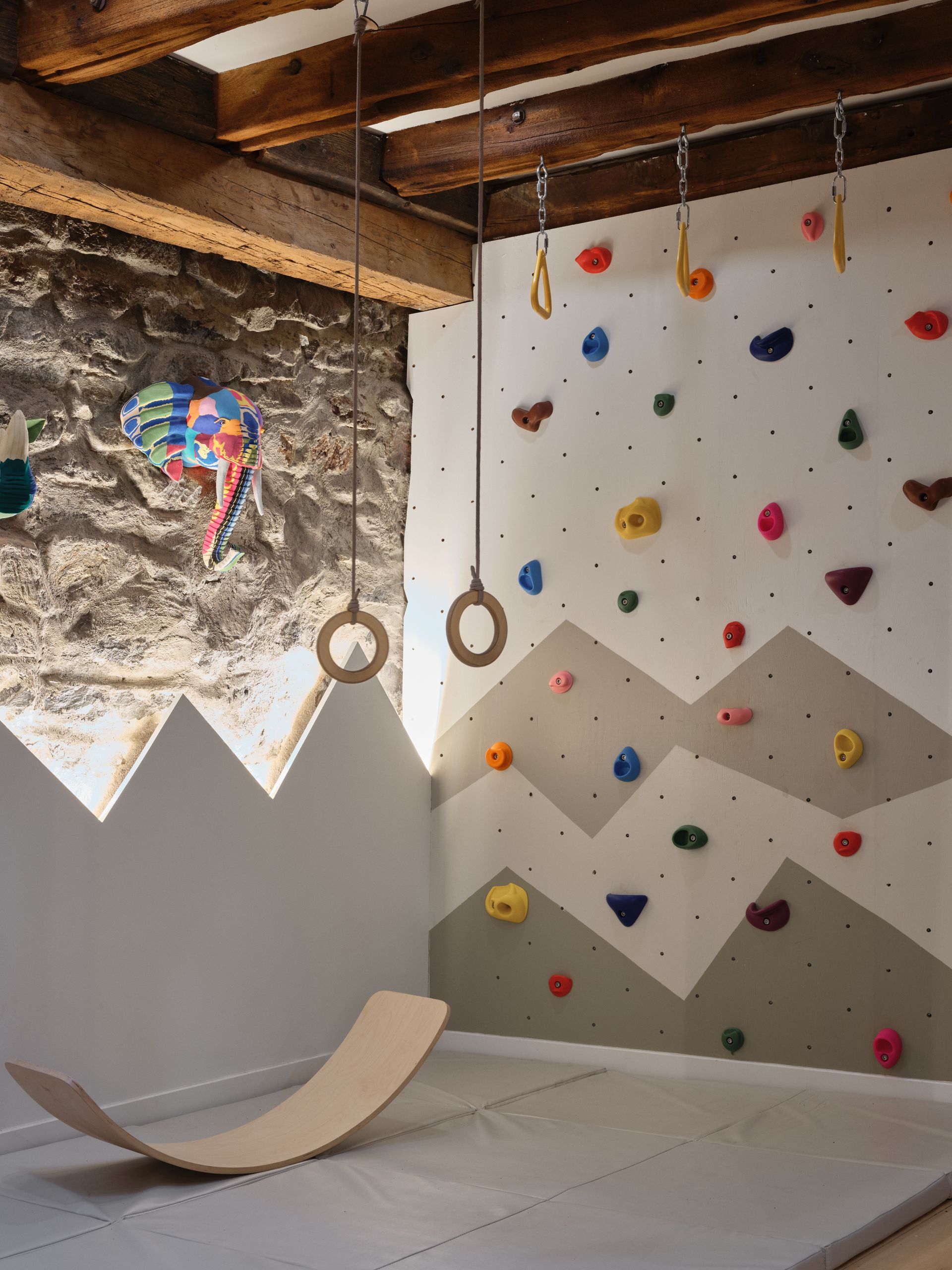 Aire de jeux intérieure avec mur d'escalade, anneaux de gymnastique et planche d'équilibre.