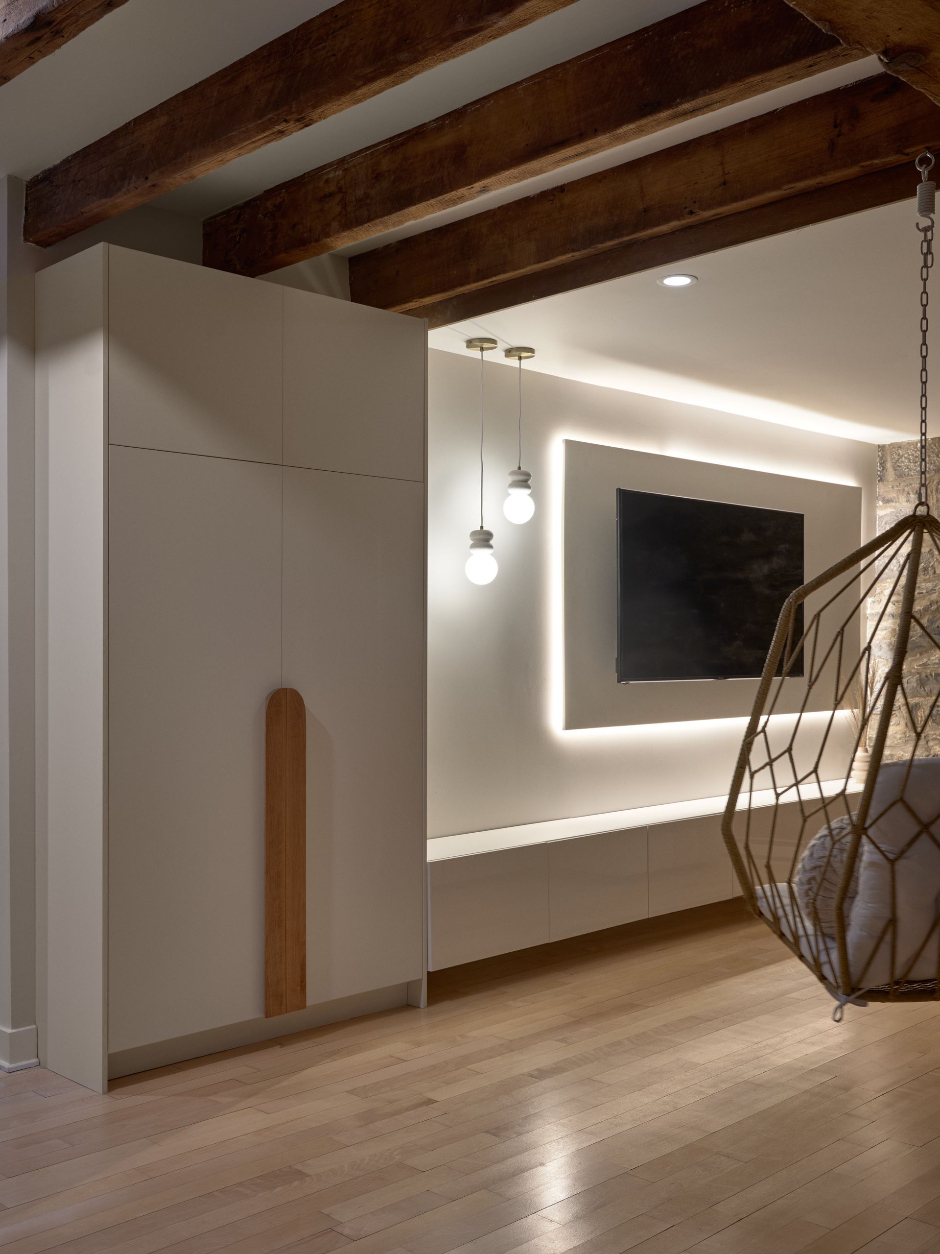 Intérieur moderne avec un meuble TV intégré, un fauteuil suspendu et des poutres apparentes.