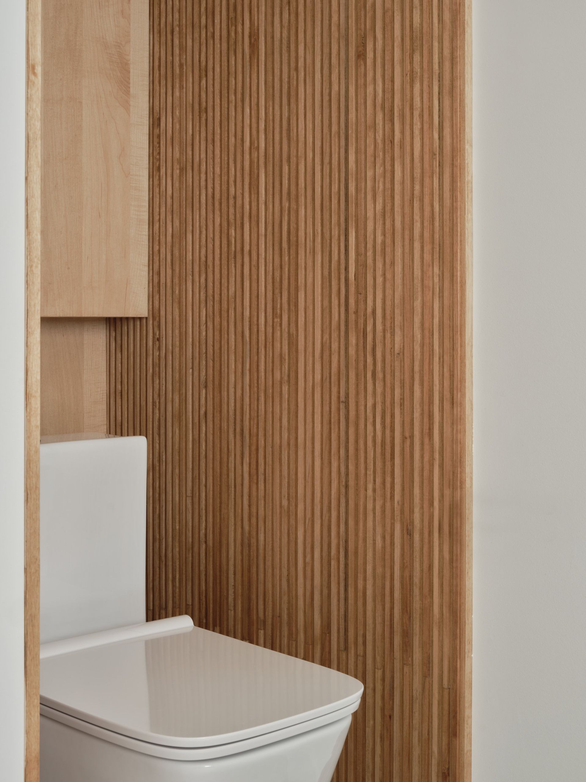 Des toilettes se trouvent dans une salle de bain à côté d'un mur en bois.