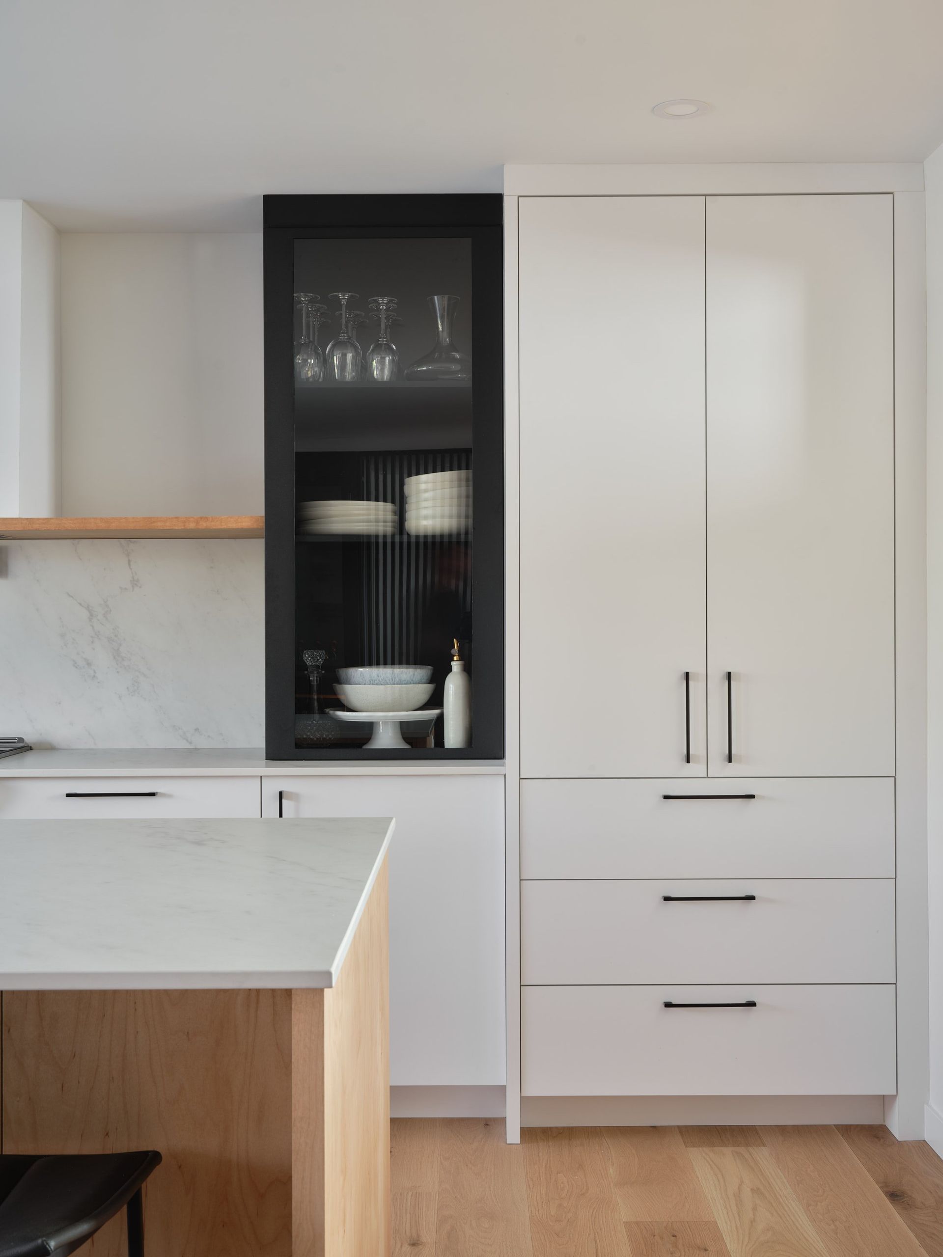 Une cuisine avec des armoires blanches, du parquet et une porte vitrée.