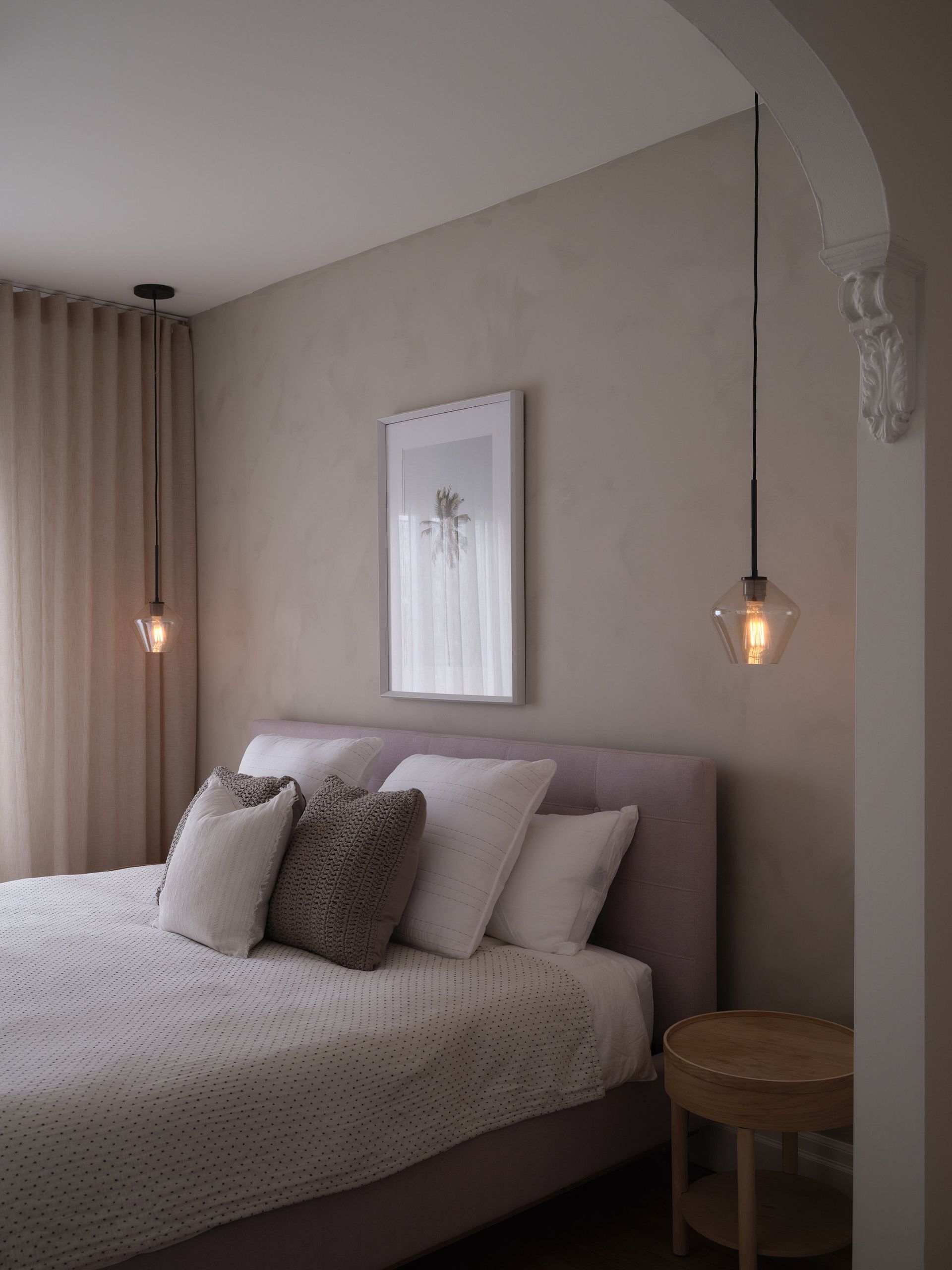 Une chambre avec un lit , une table de nuit , des lampes et un tableau au mur.