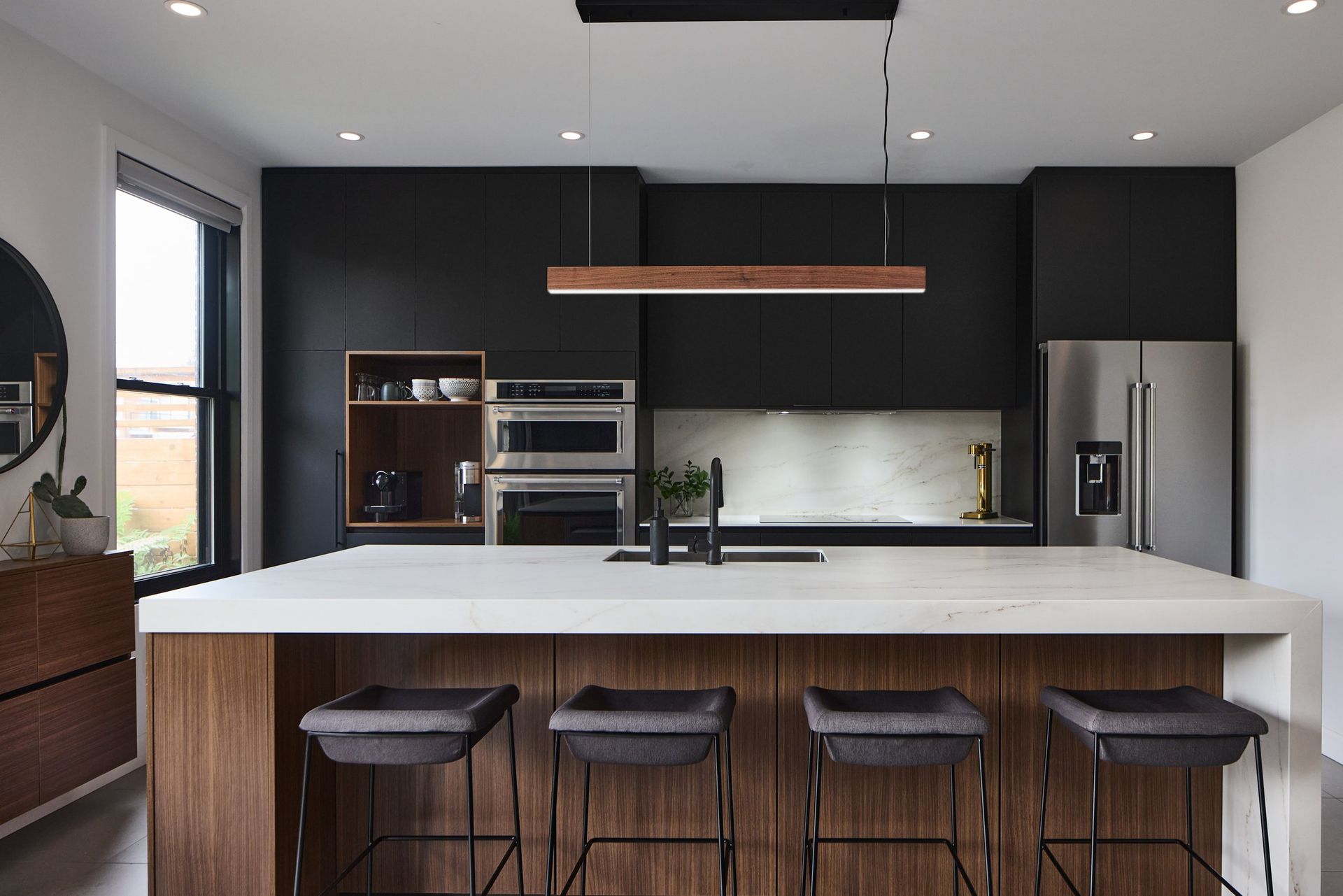 Une cuisine avec armoires noires, électroménagers en acier inoxydable, un grand îlot et des tabourets.
