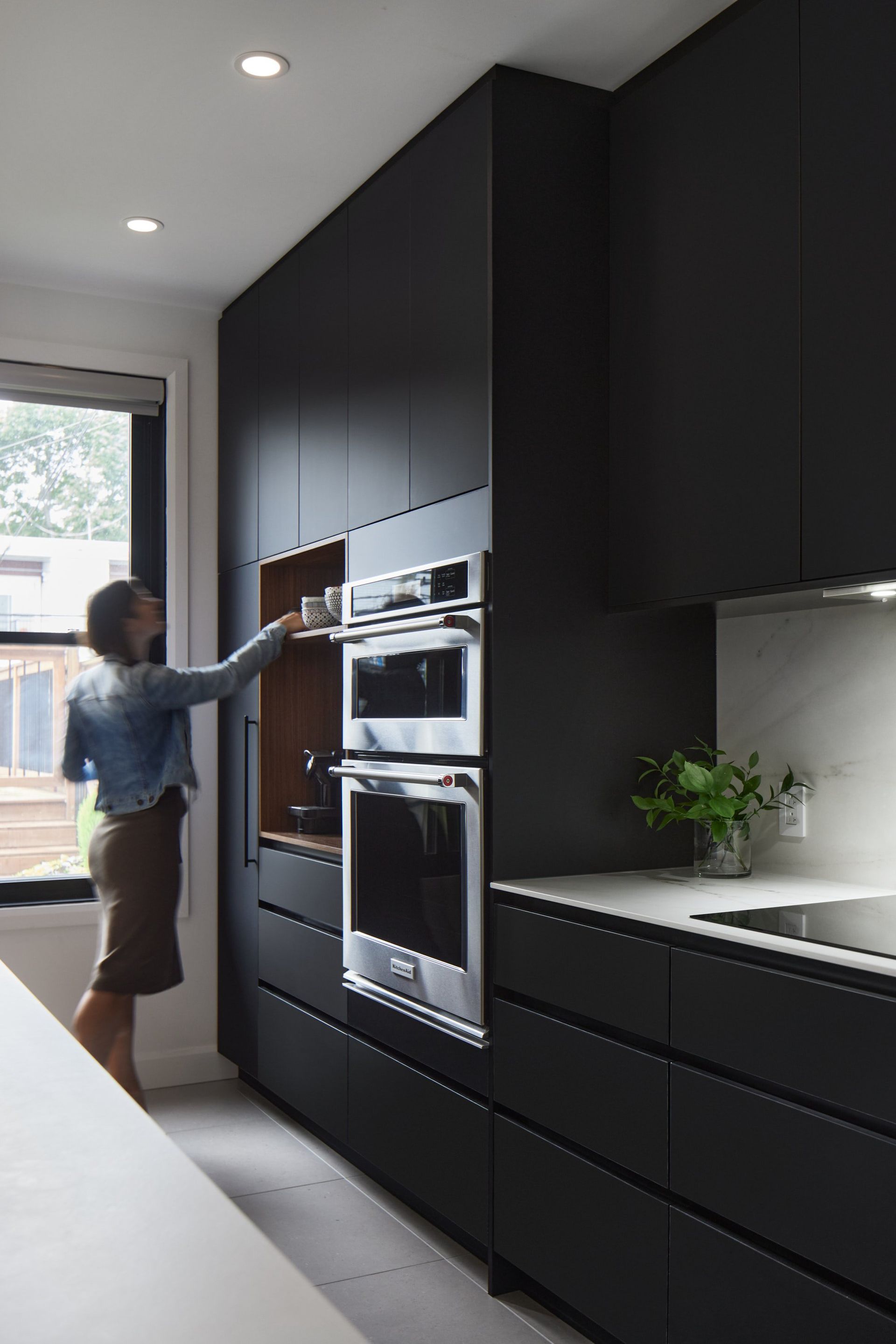 Une femme se tient debout dans une cuisine et tend la main vers un placard.
