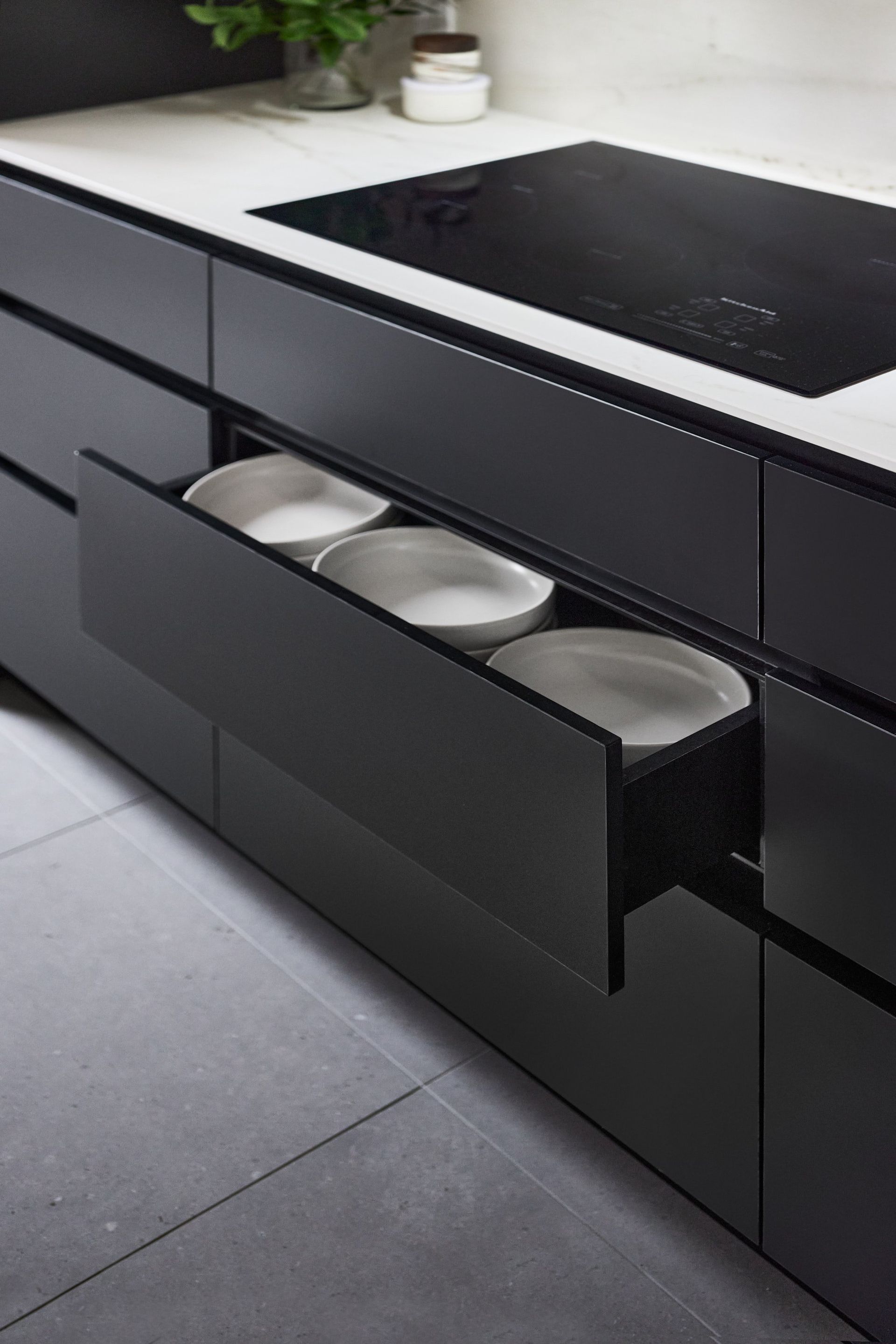 Une cuisine avec armoires noires et assiettes blanches dans les tiroirs