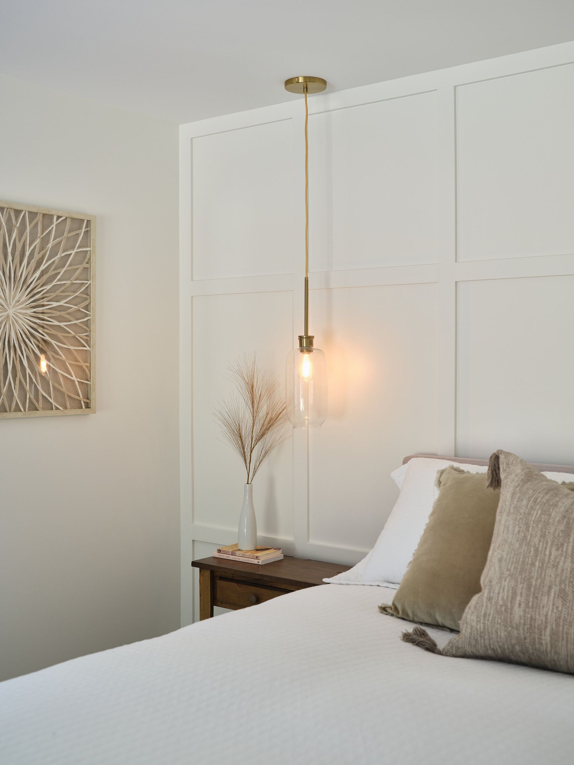 Une chambre avec un lit, une table de nuit, une lampe et un tableau au mur.