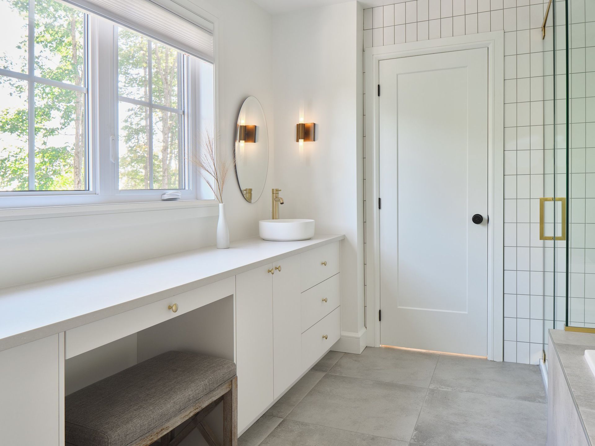 Une salle de bain avec lavabo , miroir , banquette et fenêtre.