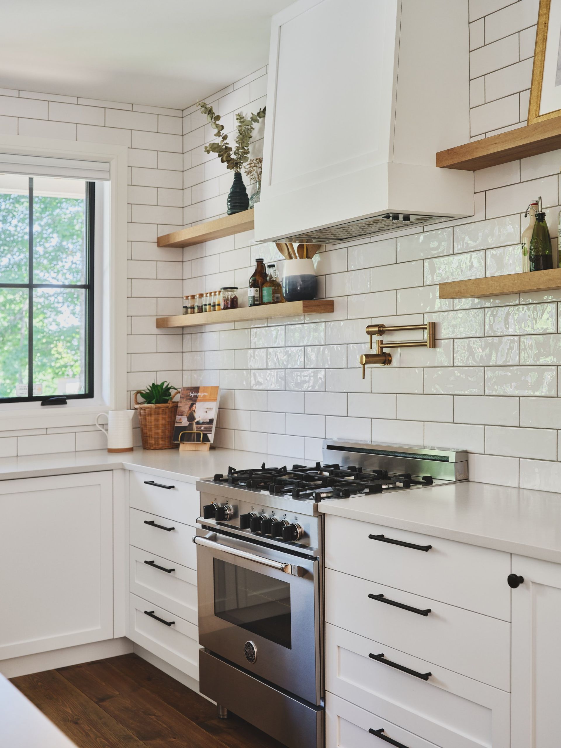 Une cuisine avec des armoires blanches, des électroménagers en acier inoxydable, une cuisinière et une fenêtre.