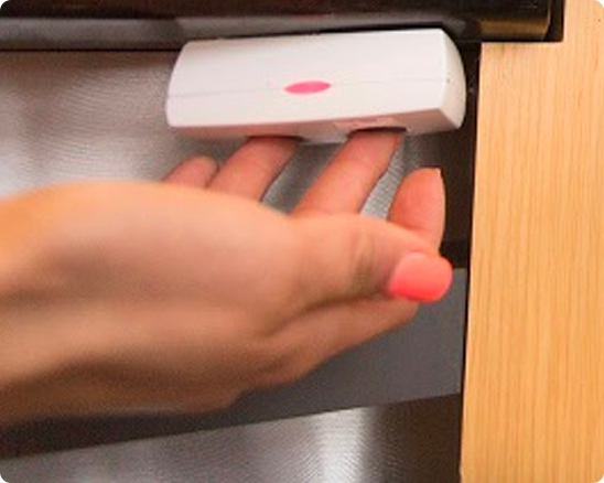 Hand reaching for a white device with a pink light installed under a cabinet.