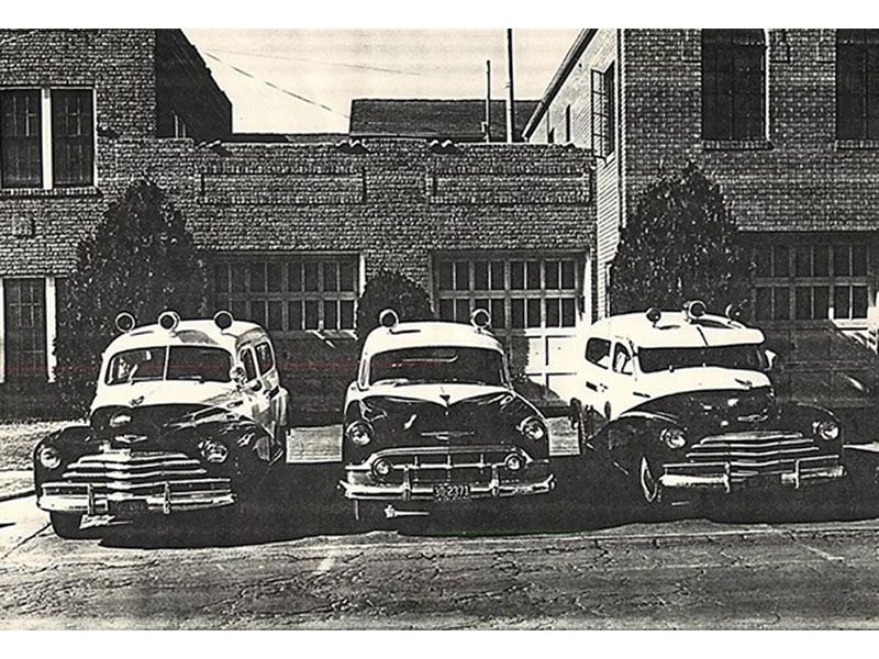 Three old cars are parked in front of a brick building