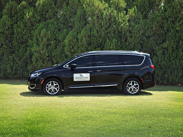 A black minivan is parked in a grassy field.