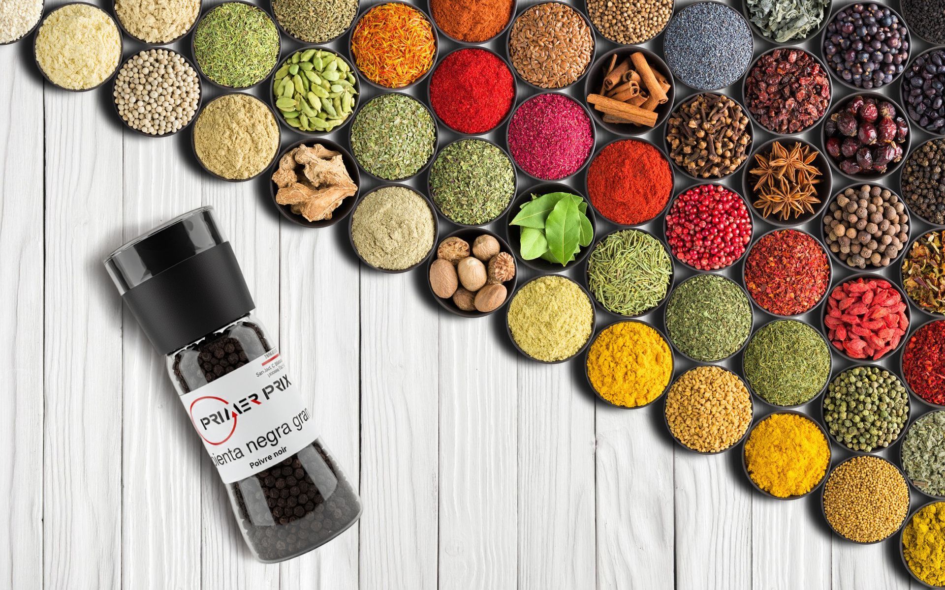 Spice shaker with pepper in front of a colorful array of spices in small bowls, arranged on a white wood surface.