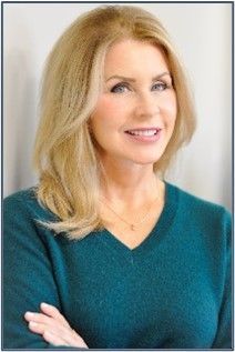 A woman in a blue sweater is smiling with her arms crossed.