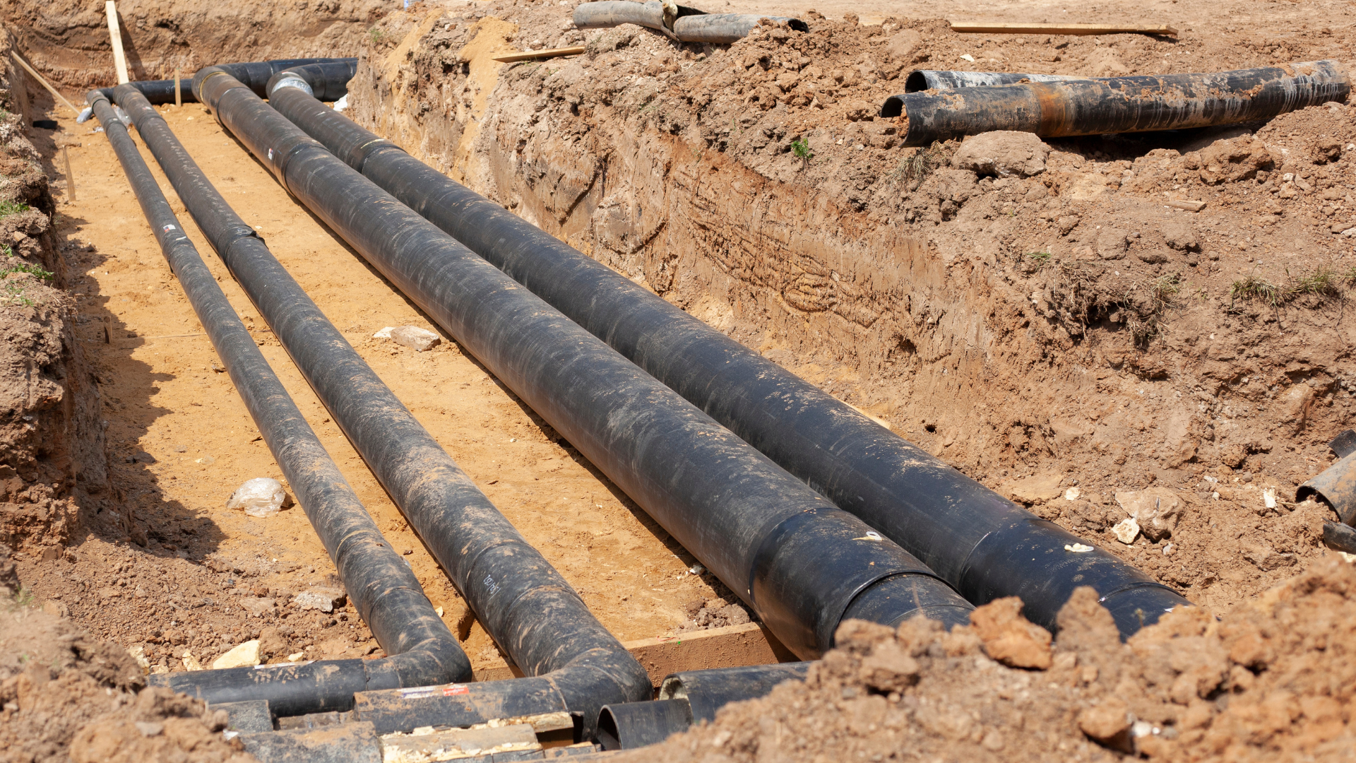 Black pipes laid in a trench, surrounded by dirt and sand, likely for utilities underground.
