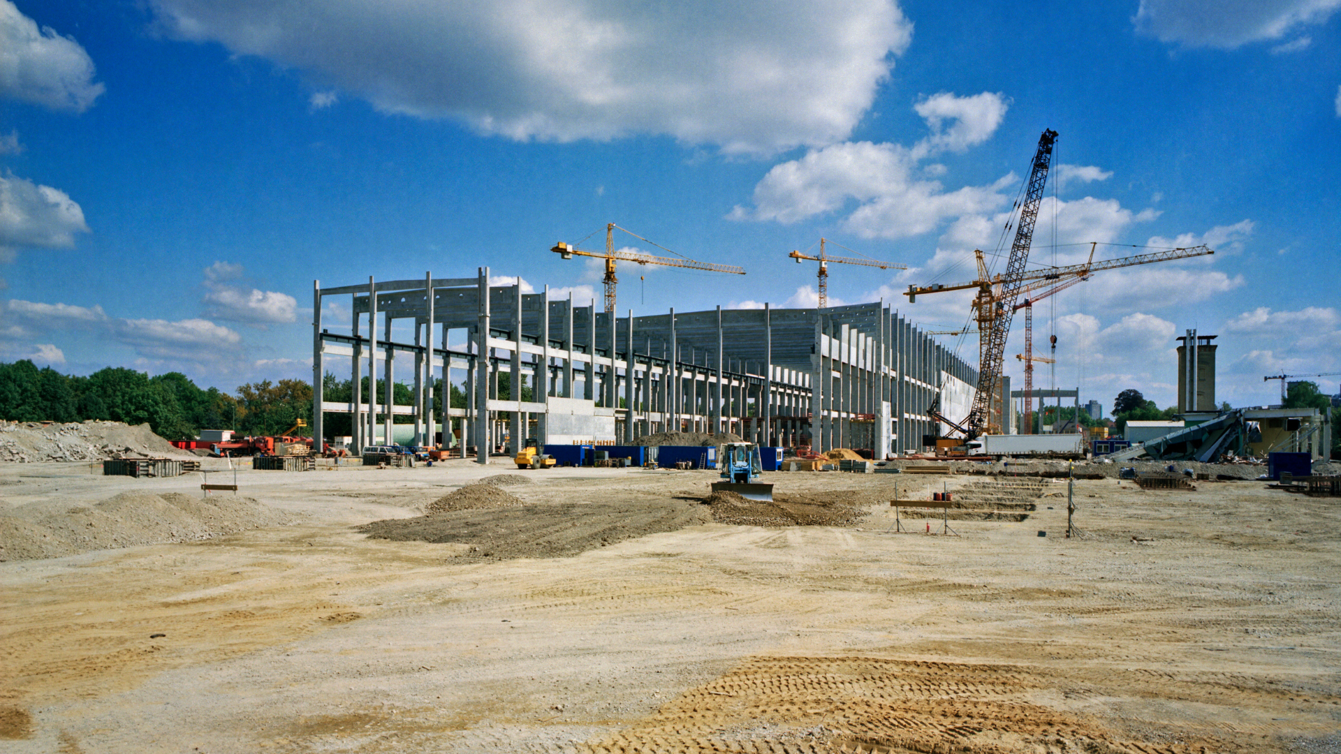 Construction site of a large building with cranes under a blue sky.